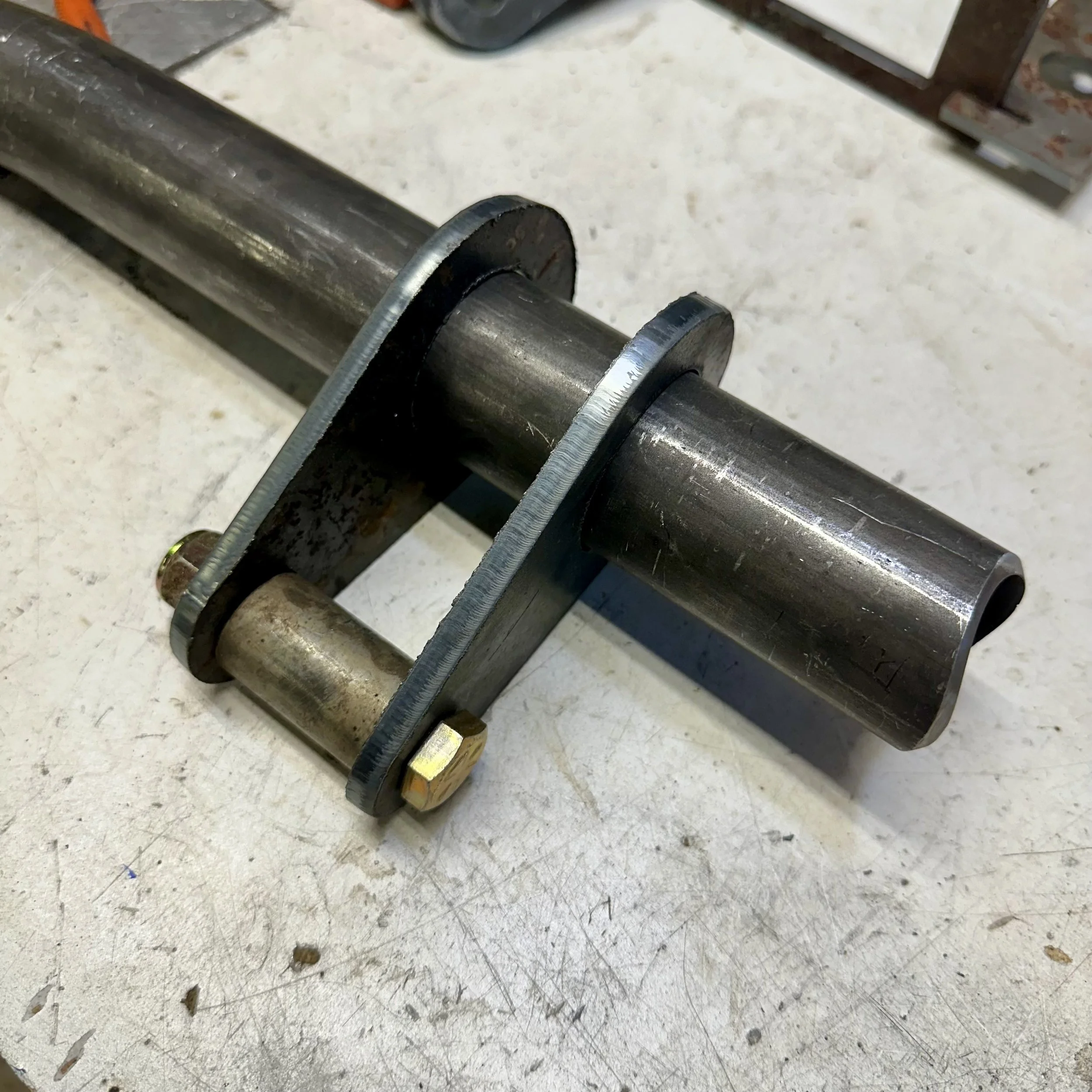 Close-up of a metal roller with a spindle, lying on a scratched work surface in a workshop.