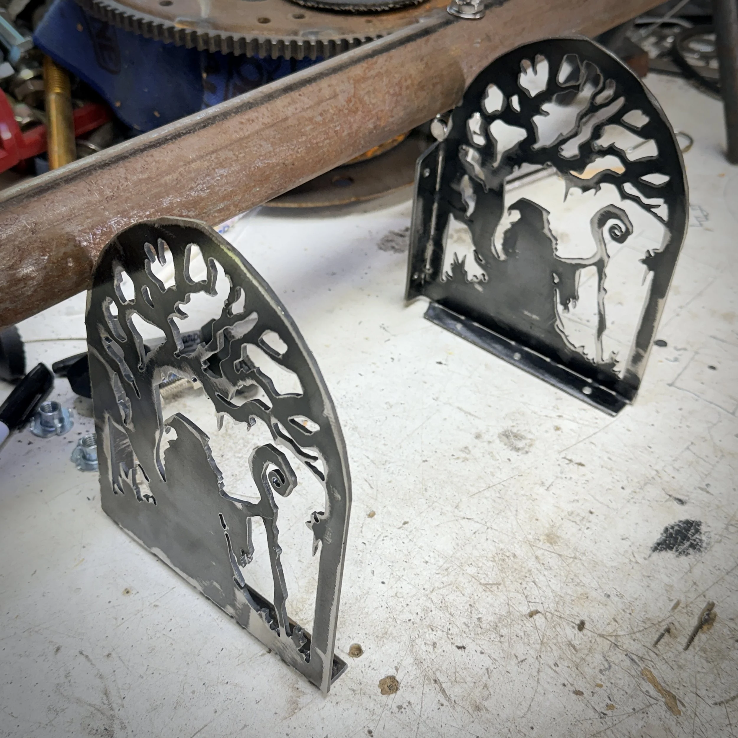 Close-up of a rusty metal gear system with black metal structures featuring cut-out animal designs, on a white workbench surface.