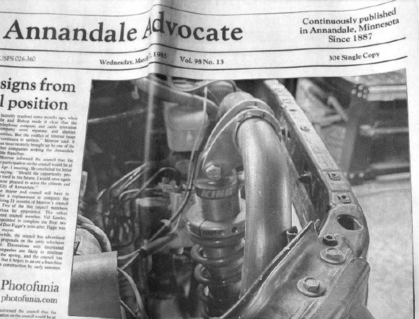 Black and white photo of a car's engine showing a coil spring and various engine components. Part of a newspaper titled 'Annandale Advocate' with visible text and date.
