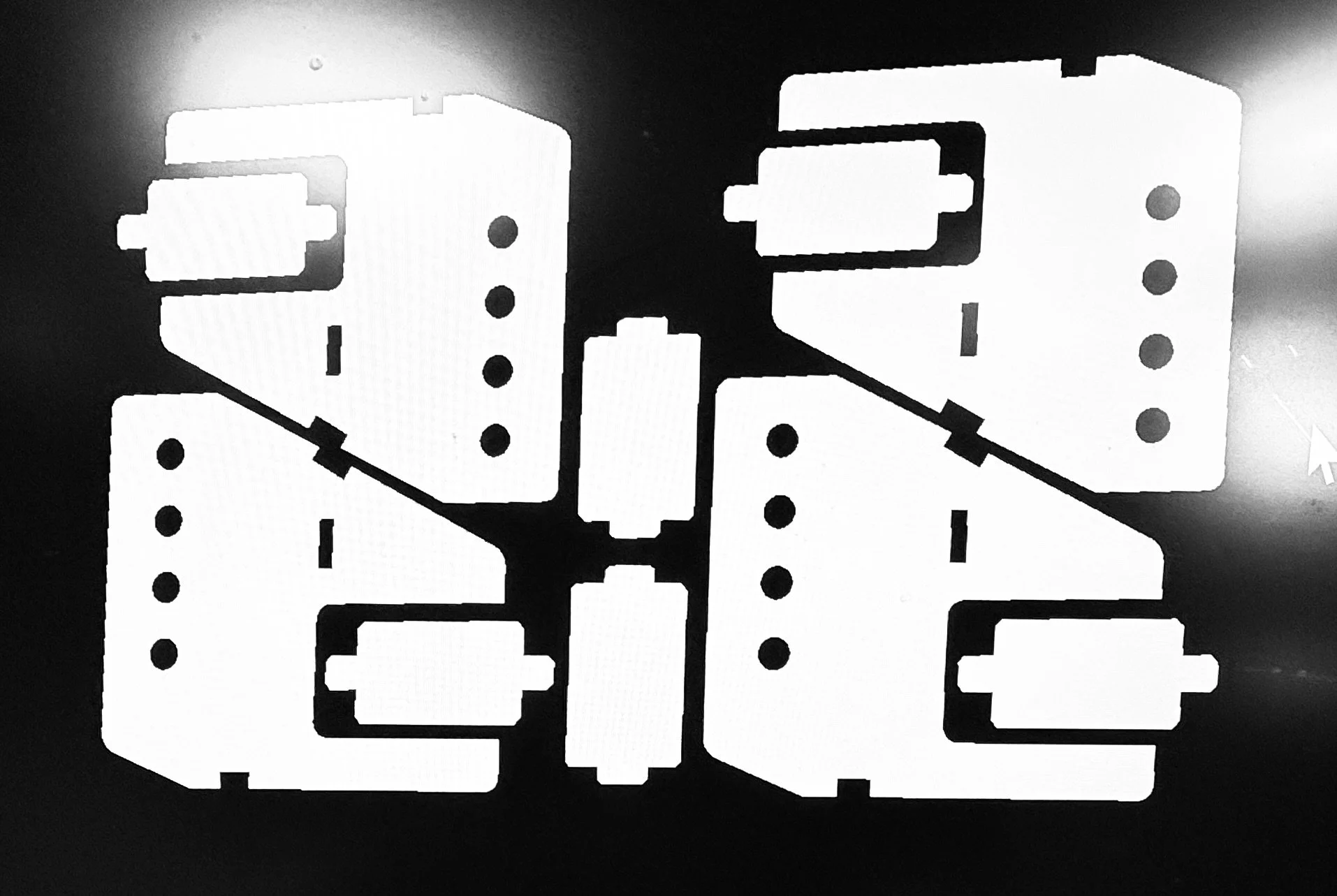 Black and white image of a mechanical or electronic component with cutouts and holes, laid against a dark background.