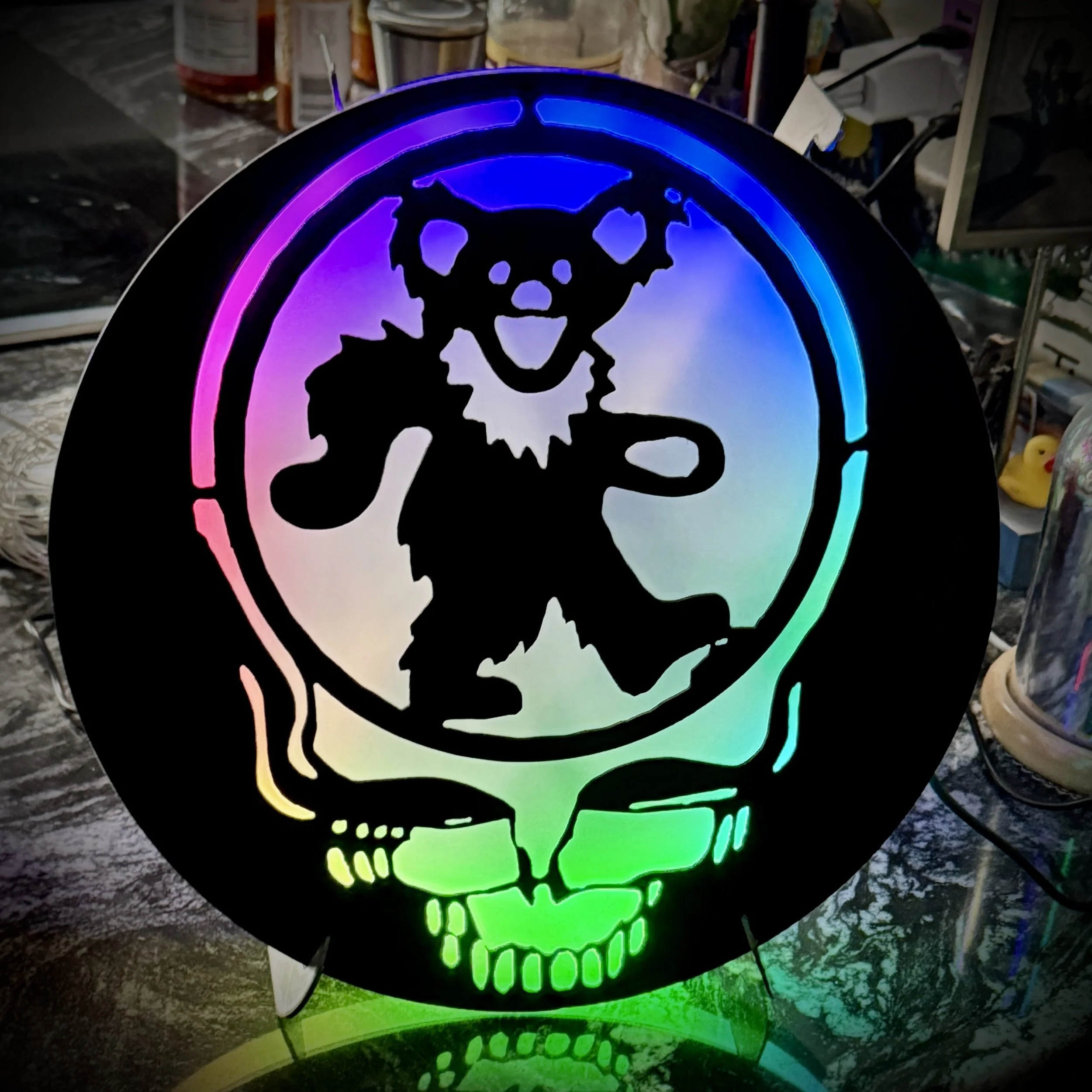 Colorful neon skull design with rainbow hues on a black background, placed outdoors on a stand.