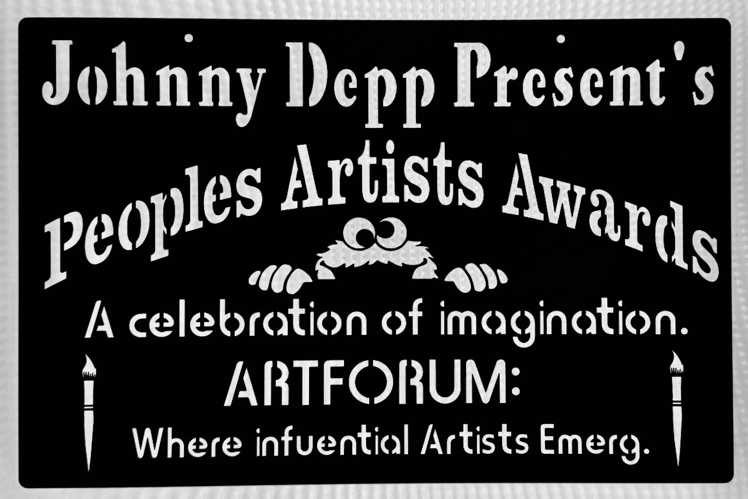 A black sign with white text promoting Johnny Depp presents the People Artists Award with a decorative flourish and stylized text.