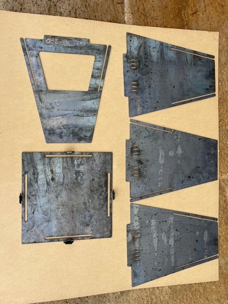 Five metal pieces, four triangular and one square, laid out on a flat surface, likely parts of a metal working project.