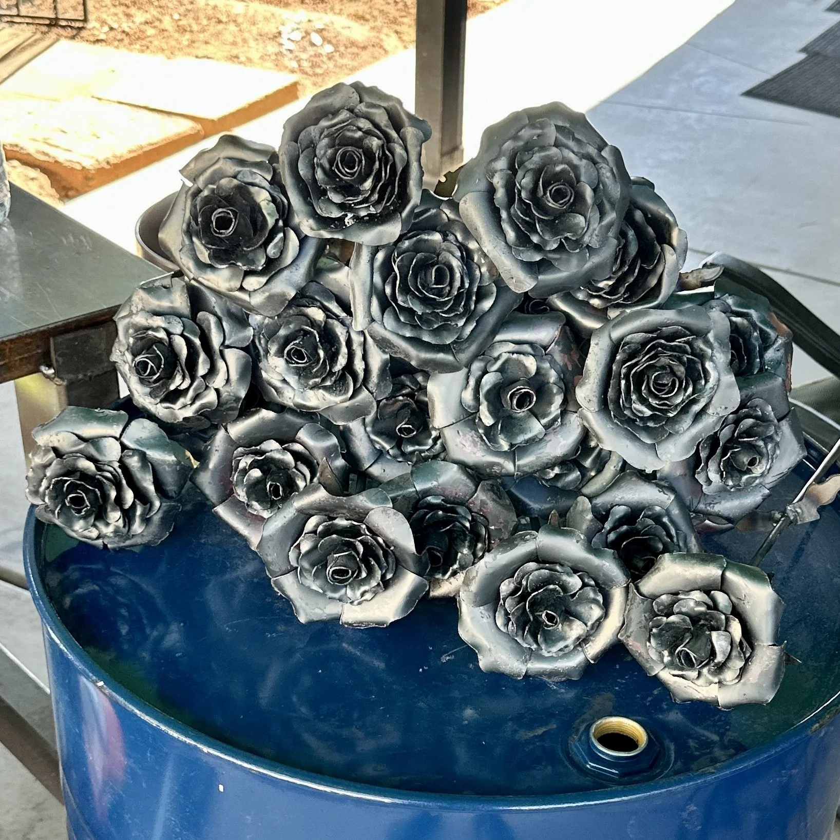 A bouquet of metal roses placed in a blue container outdoors.