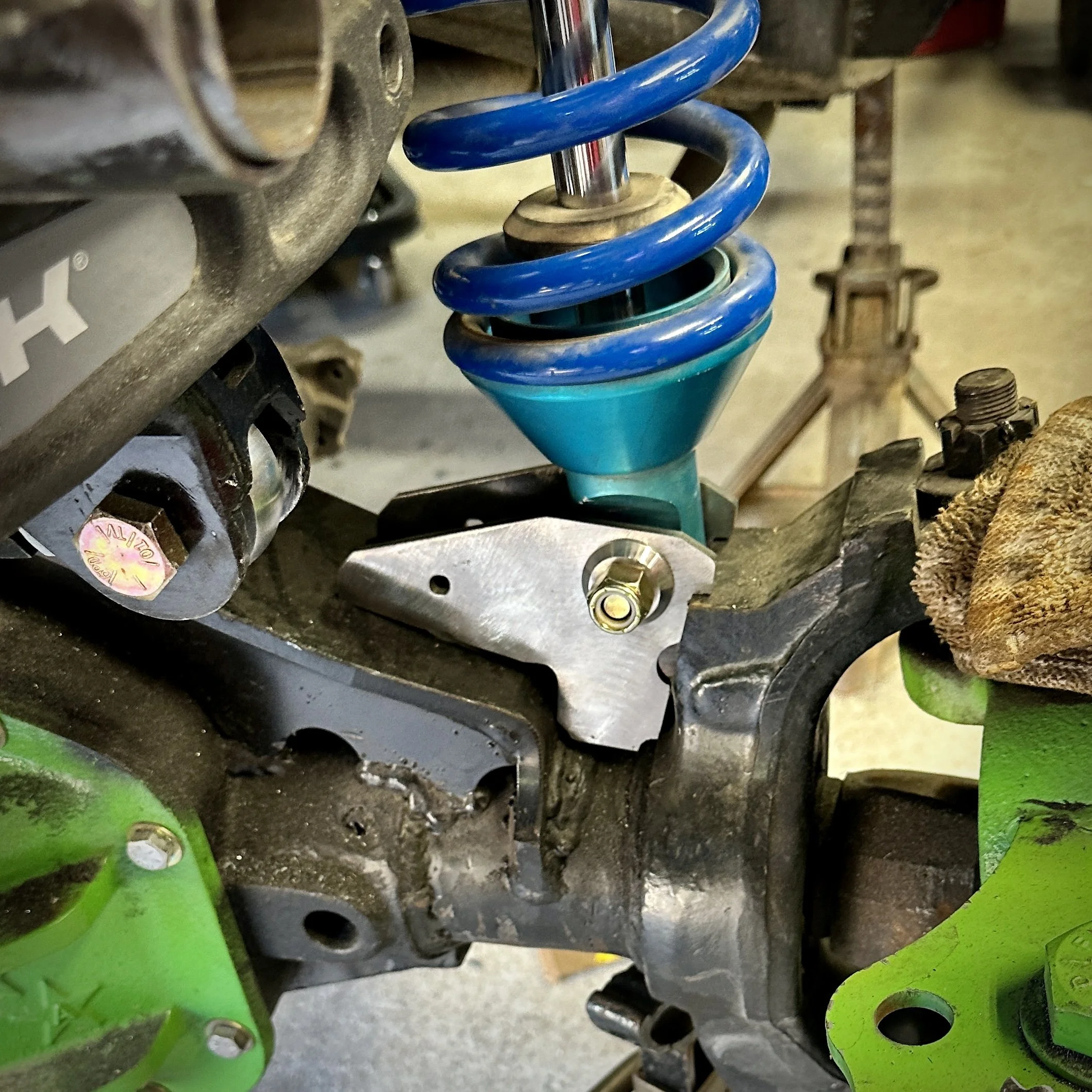 Close-up of a vehicle suspension coil spring and shock absorber assembly, with visible tire and chassis components nearby.