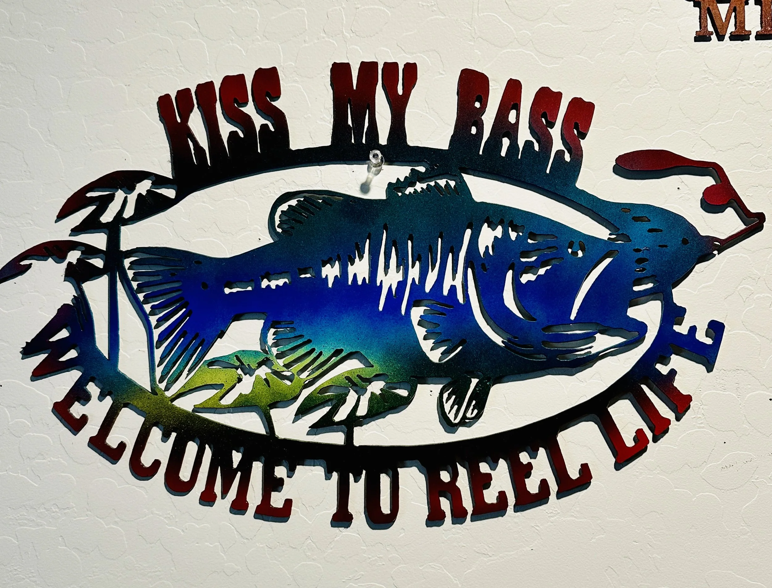 A decorative sign featuring a stylized fish surrounded by text that reads "Kiss My Bass."