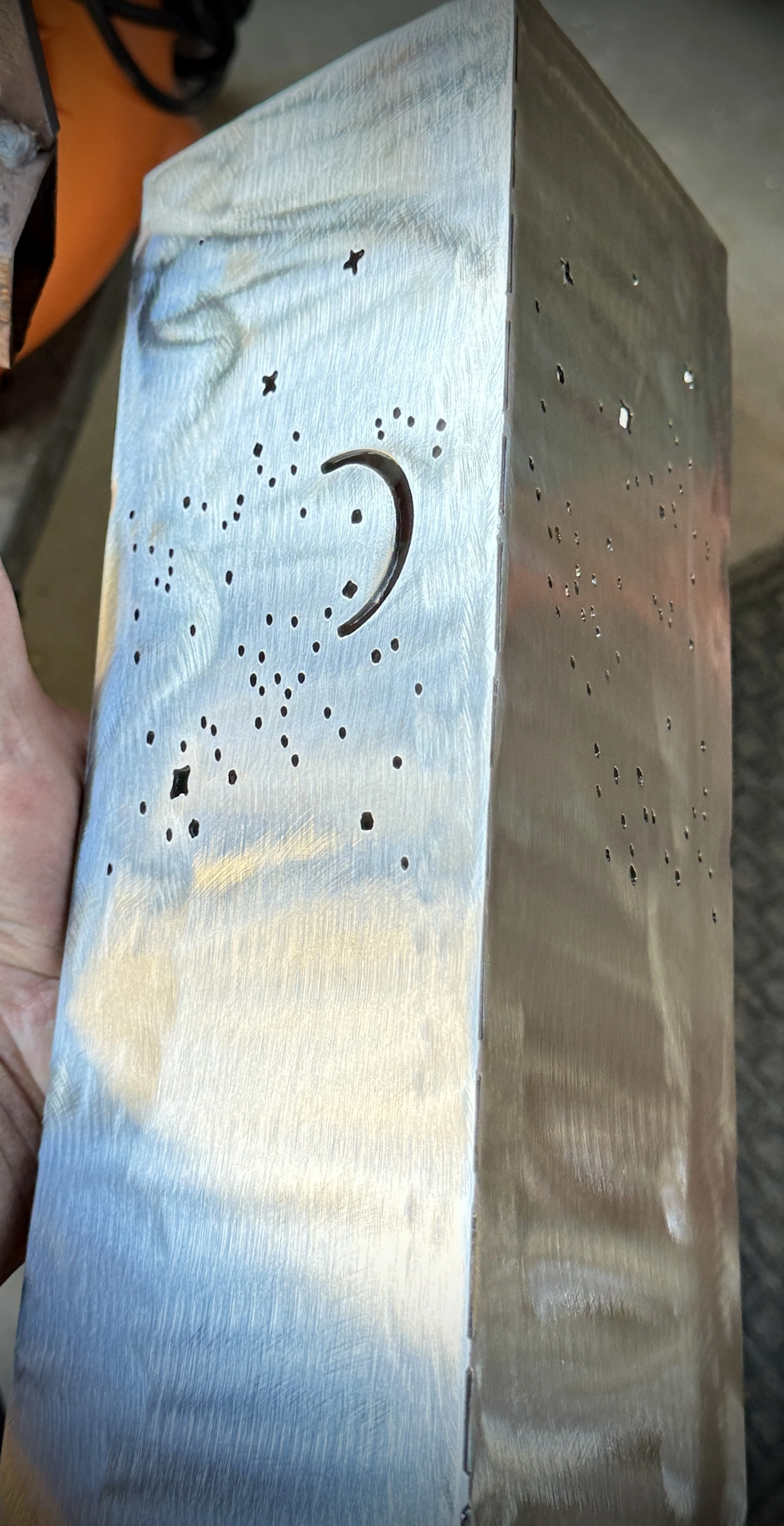 Close-up of a metallic object with a moon and star design, featuring numerous small holes for ventilation or decoration, held in a person's hand.