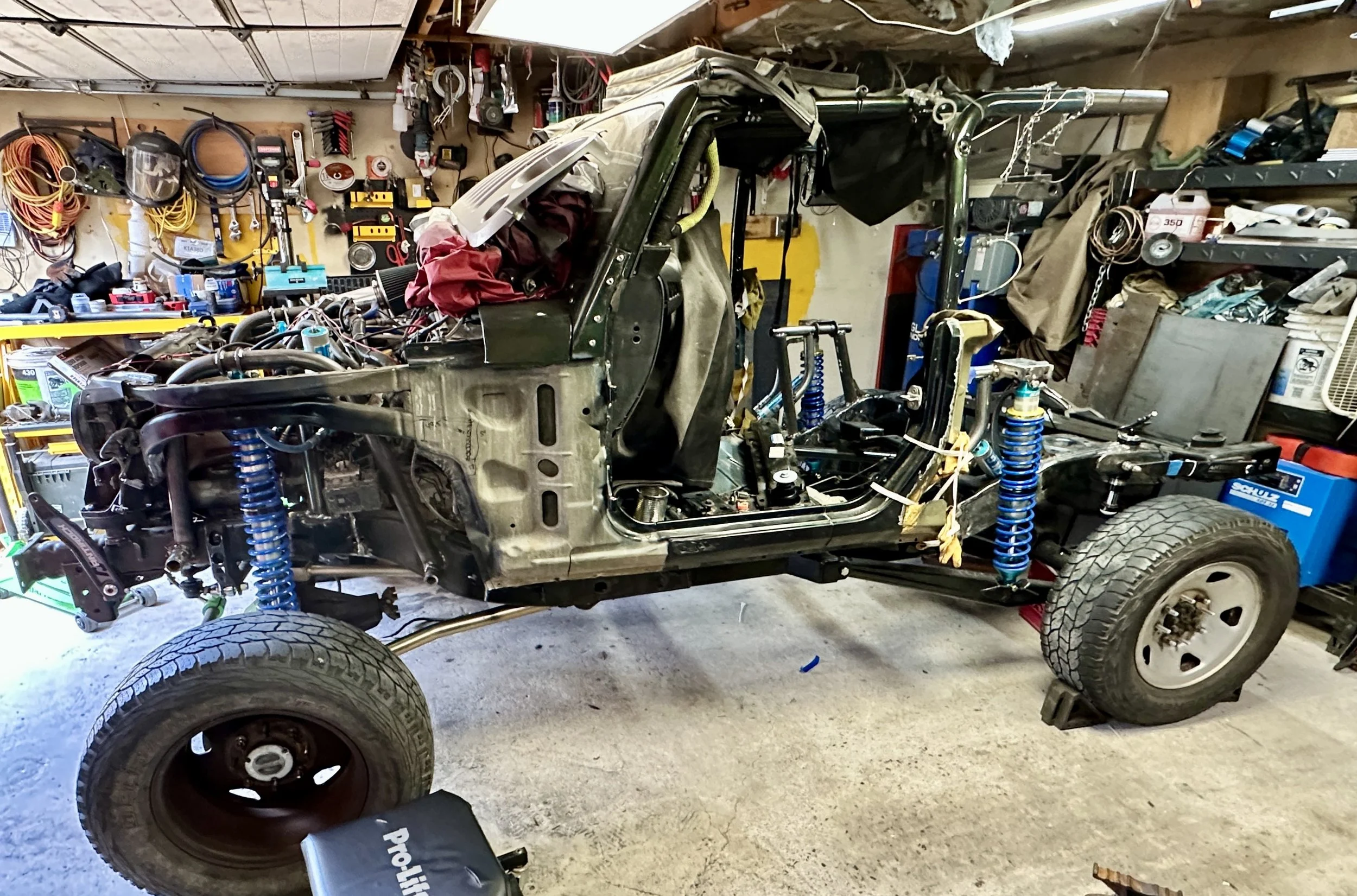 A partially disassembled off-road vehicle in a garage with tools, parts, and equipment on shelves and walls.