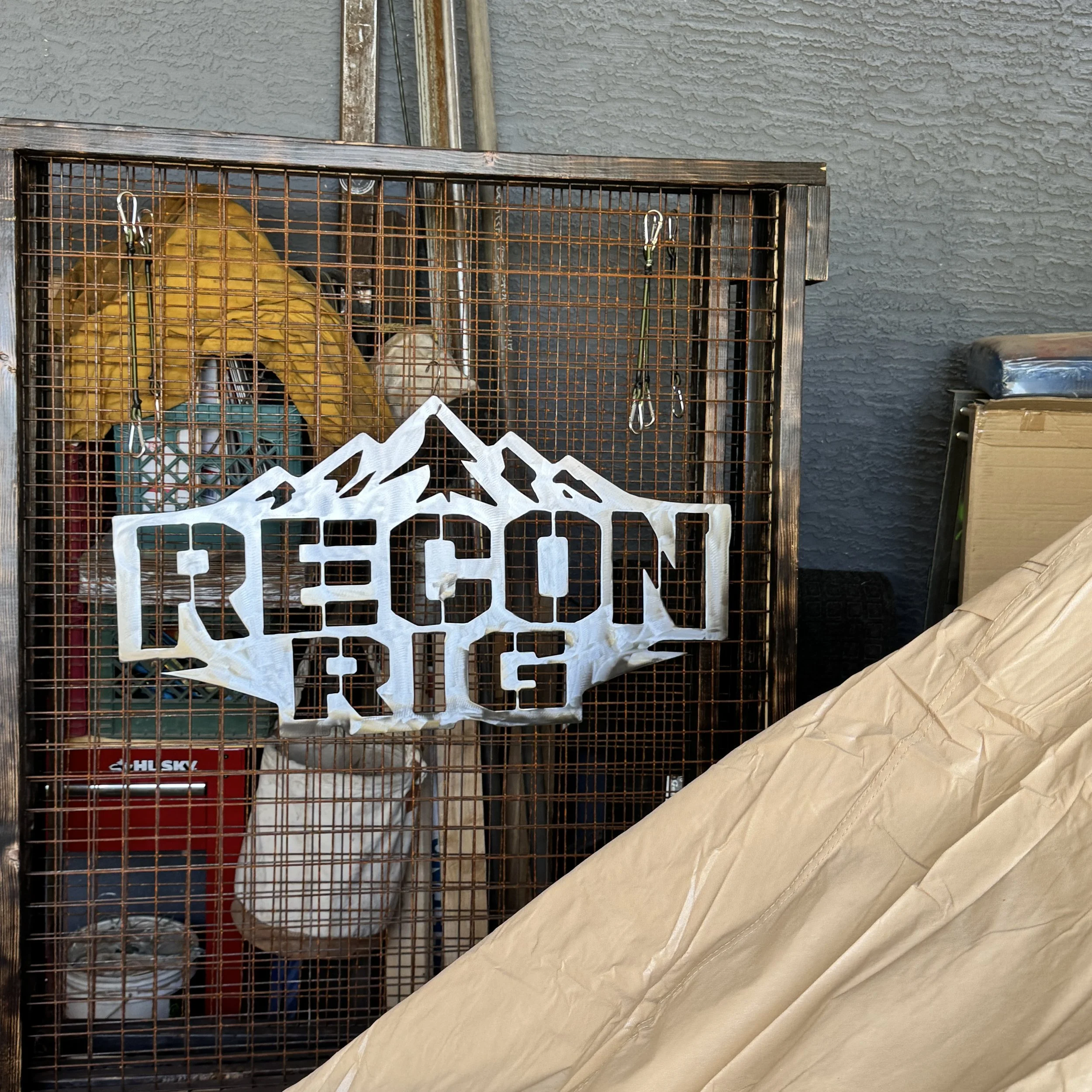 Image of a metal cage with a yellow bag inside, placed against a dark gray textured wall, with some fold paper in the foreground.