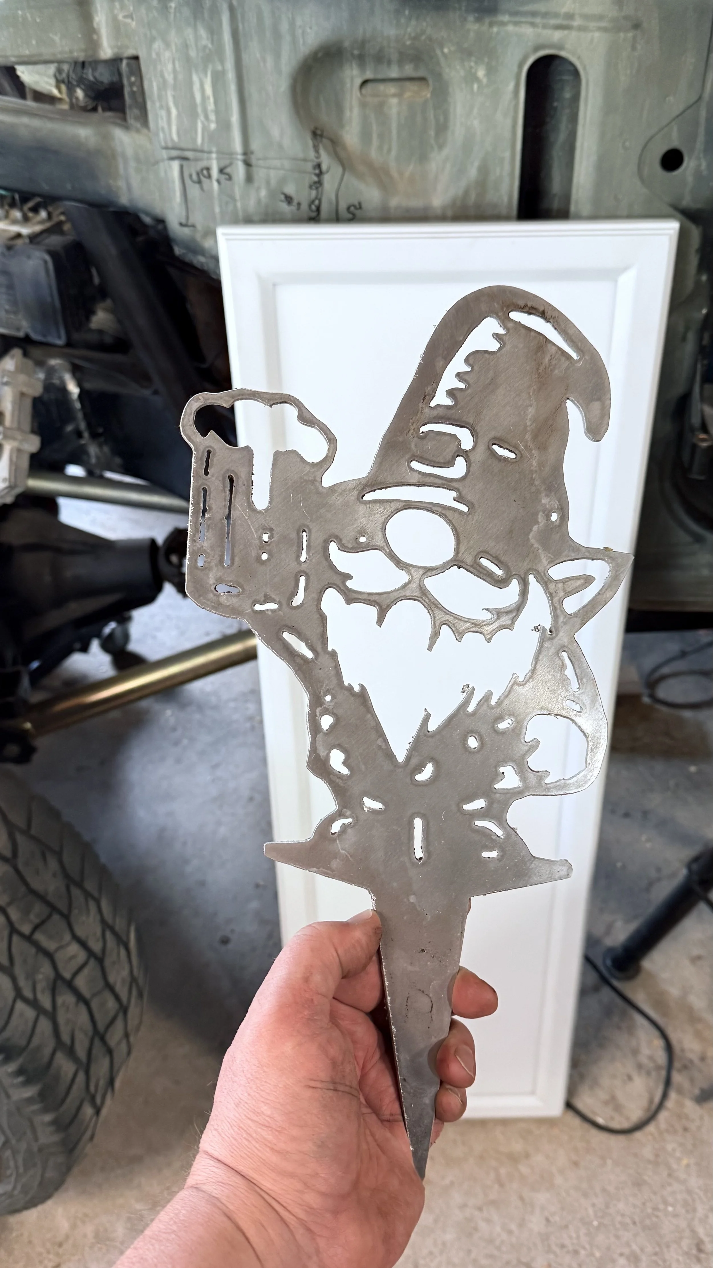 Metal cutout sculpture of a dog with a skull face being held in a person's hand.