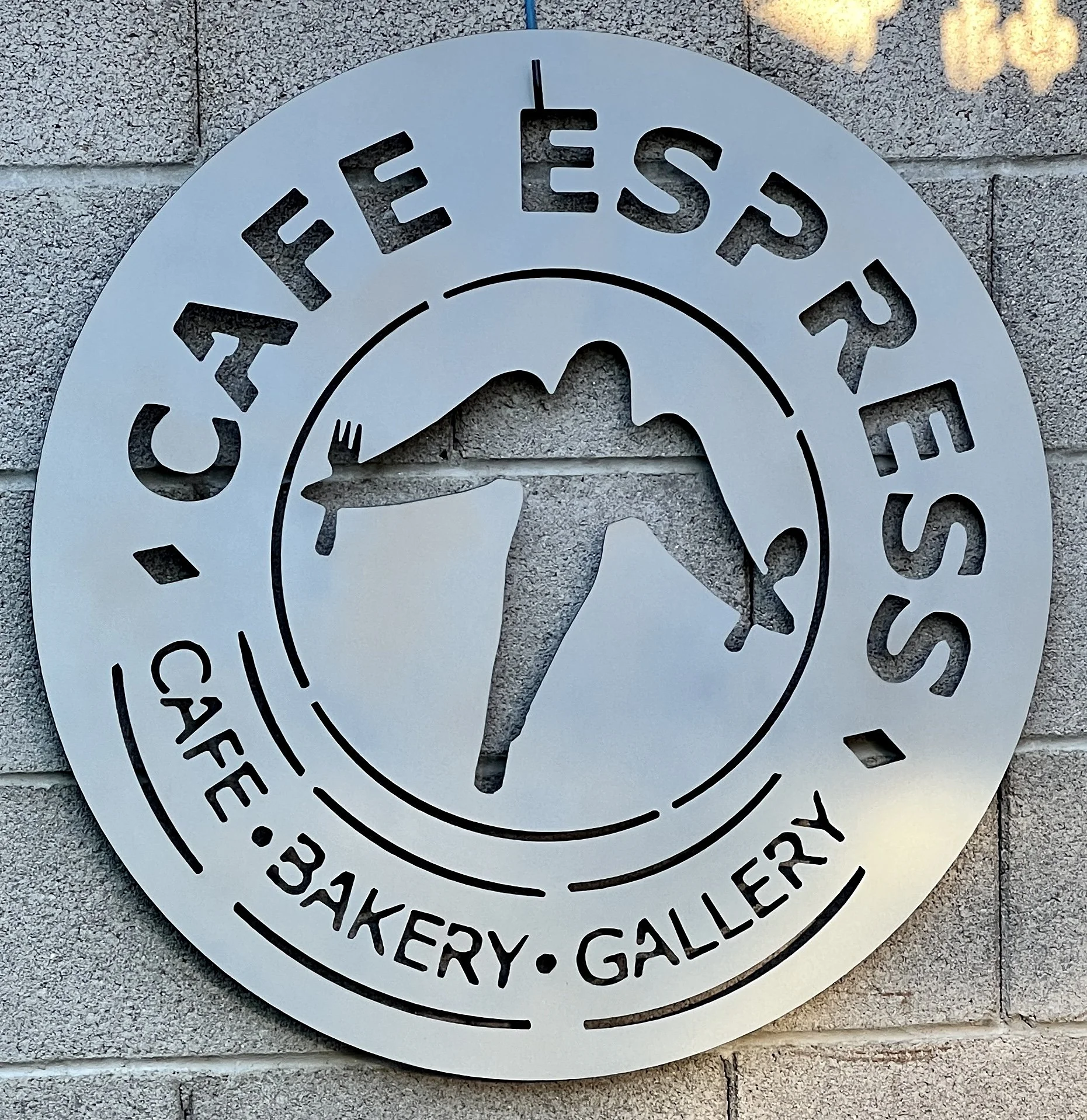 White circular sign with cut-out black text and mountain logo, hanging on a brick wall, reading 'Cheeseburger' and other words that are partially visible.