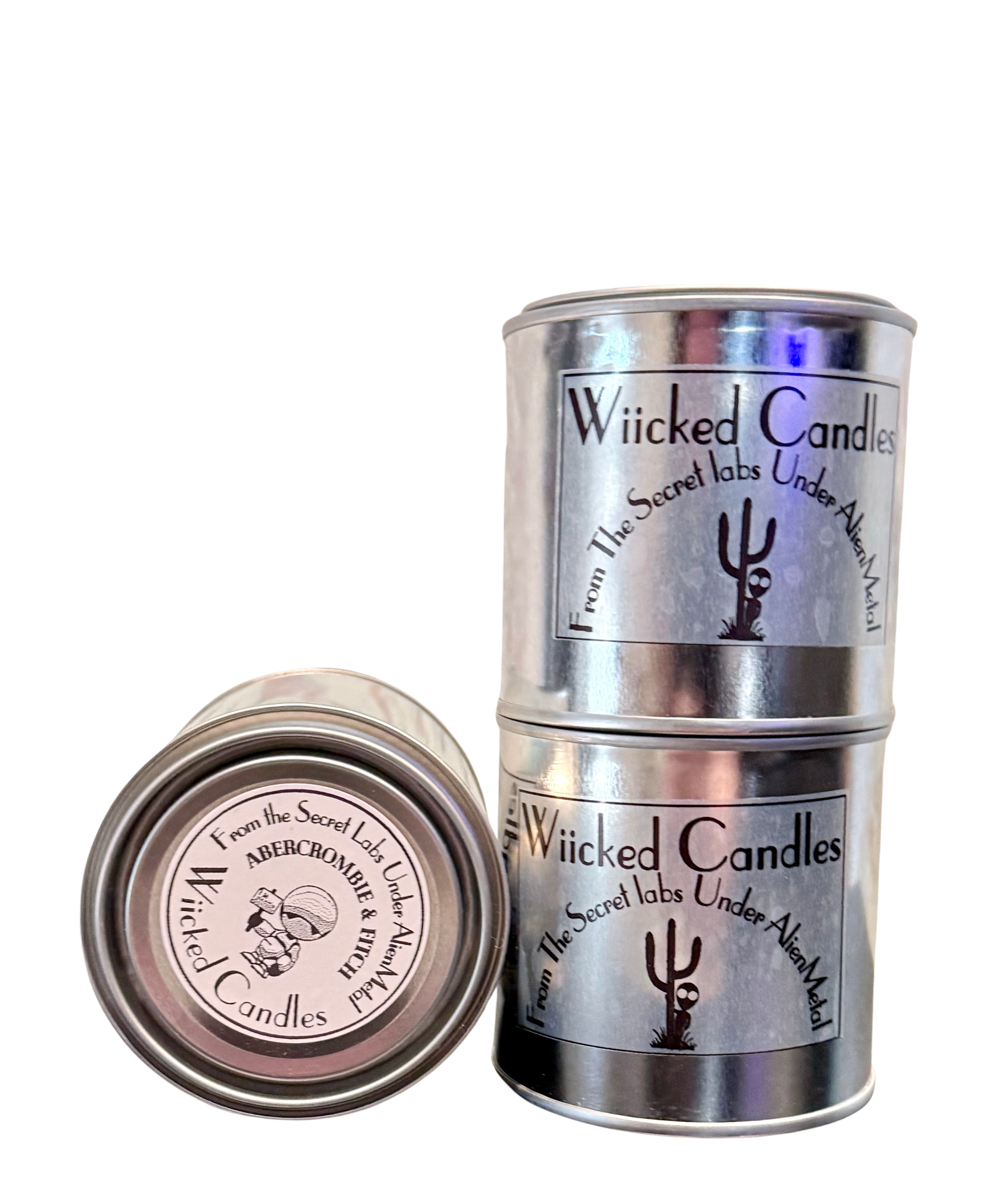 Two metal tins of Wicked Candles labeled as from the Secret Labs under Aleyen. One tin is upright with a label showing a black ghost and stylized text, the other is lying flat, revealing its lid with similar branding.