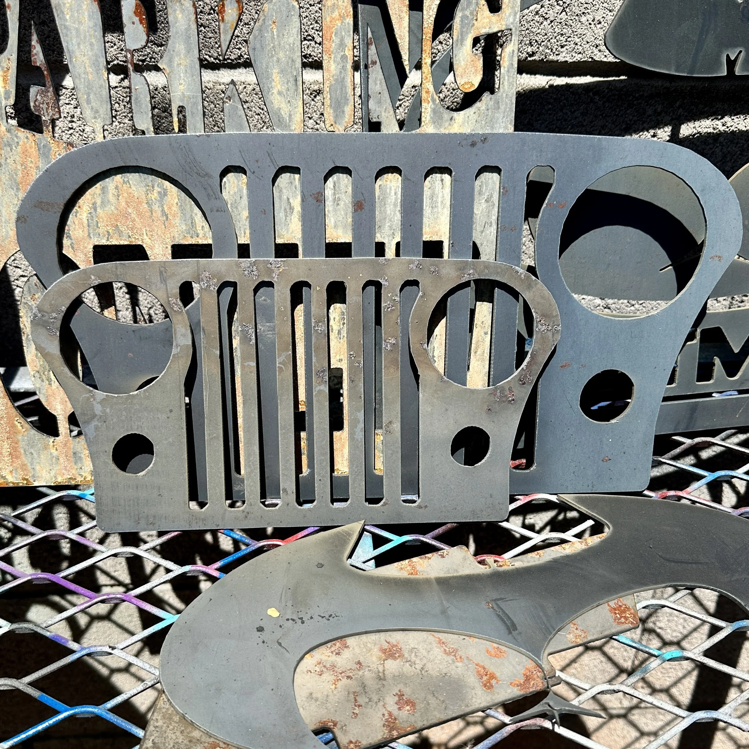 Rusty metal signs in the shape of a Jeep and the word 'RELIANCE' on a metal grid surface.