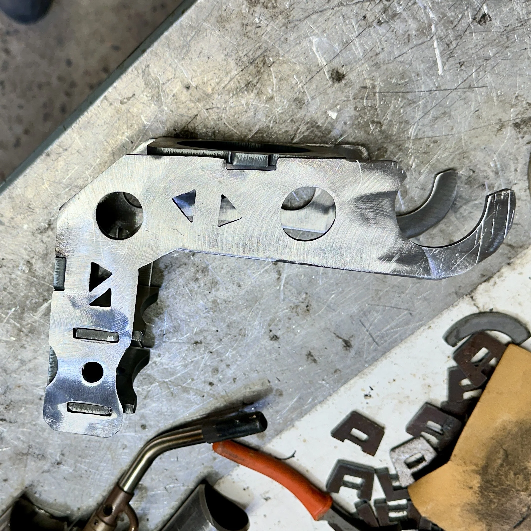 A collection of metal tools with various shapes and sizes, resting on a workbench with scratches, stains, and debris.