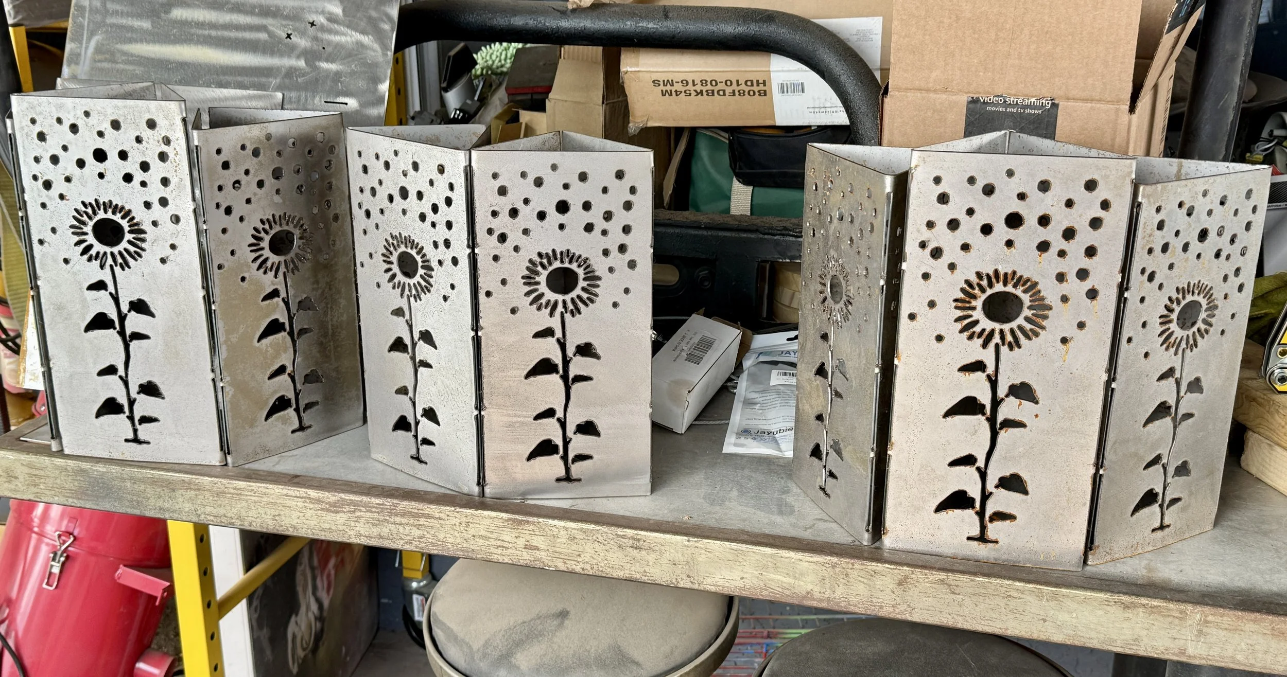 Metal folding screens with sunflower cutouts and decorative holes, displayed on a shelf at a store.