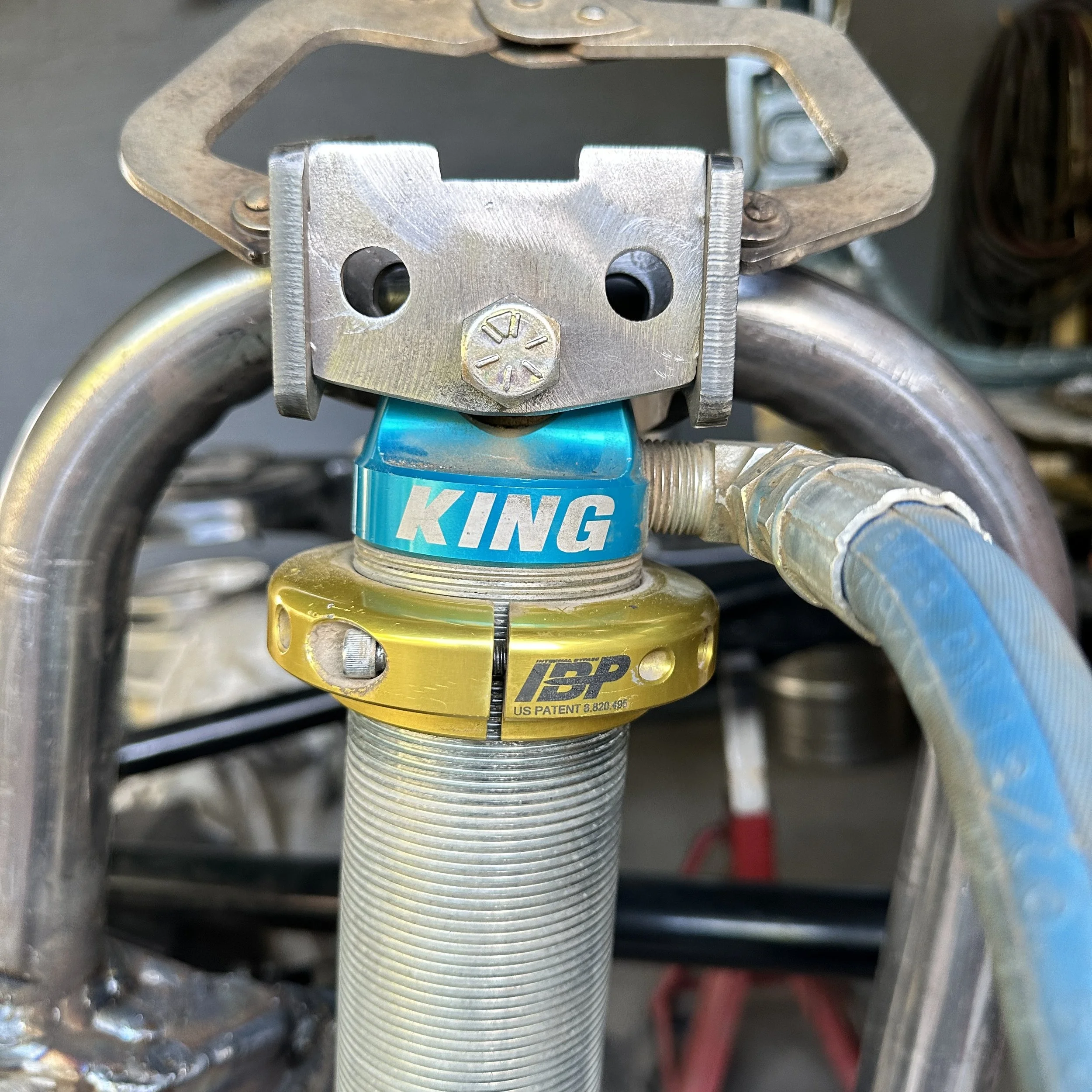 Close-up of a metal motorcycle suspension component with a blue King shock absorber labeled with a patent number, surrounded by metal parts and wires.