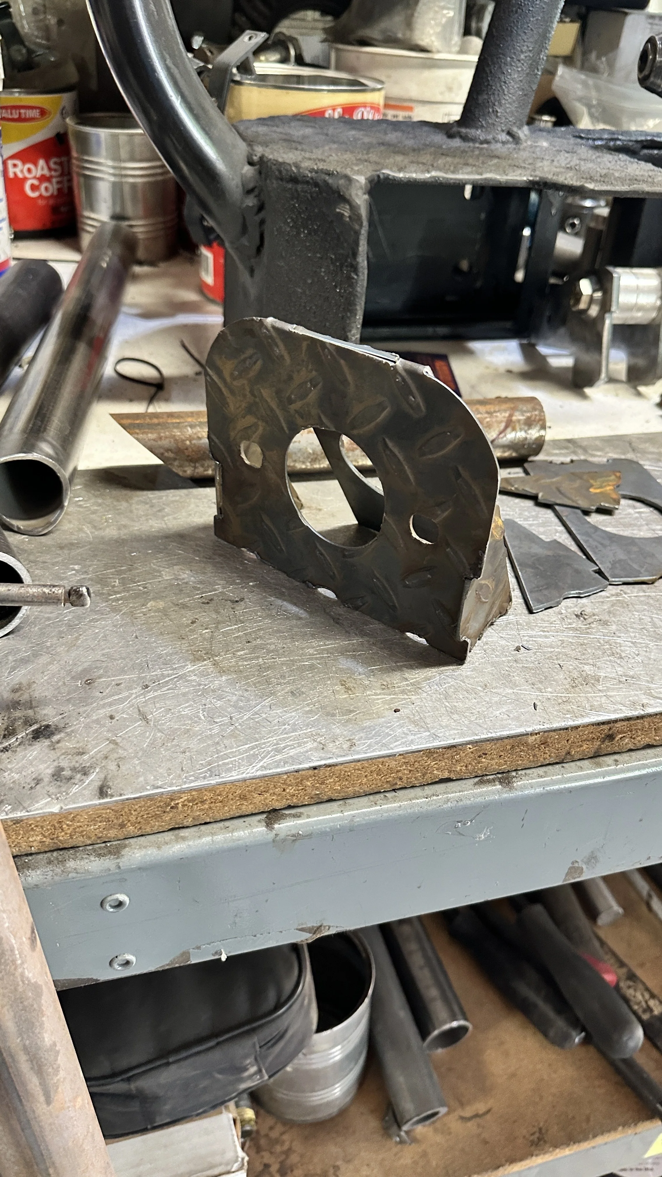 A metal workbench with various tools and metal parts, including a metal component with a circular hole and embossed patterns, in a workshop setting.