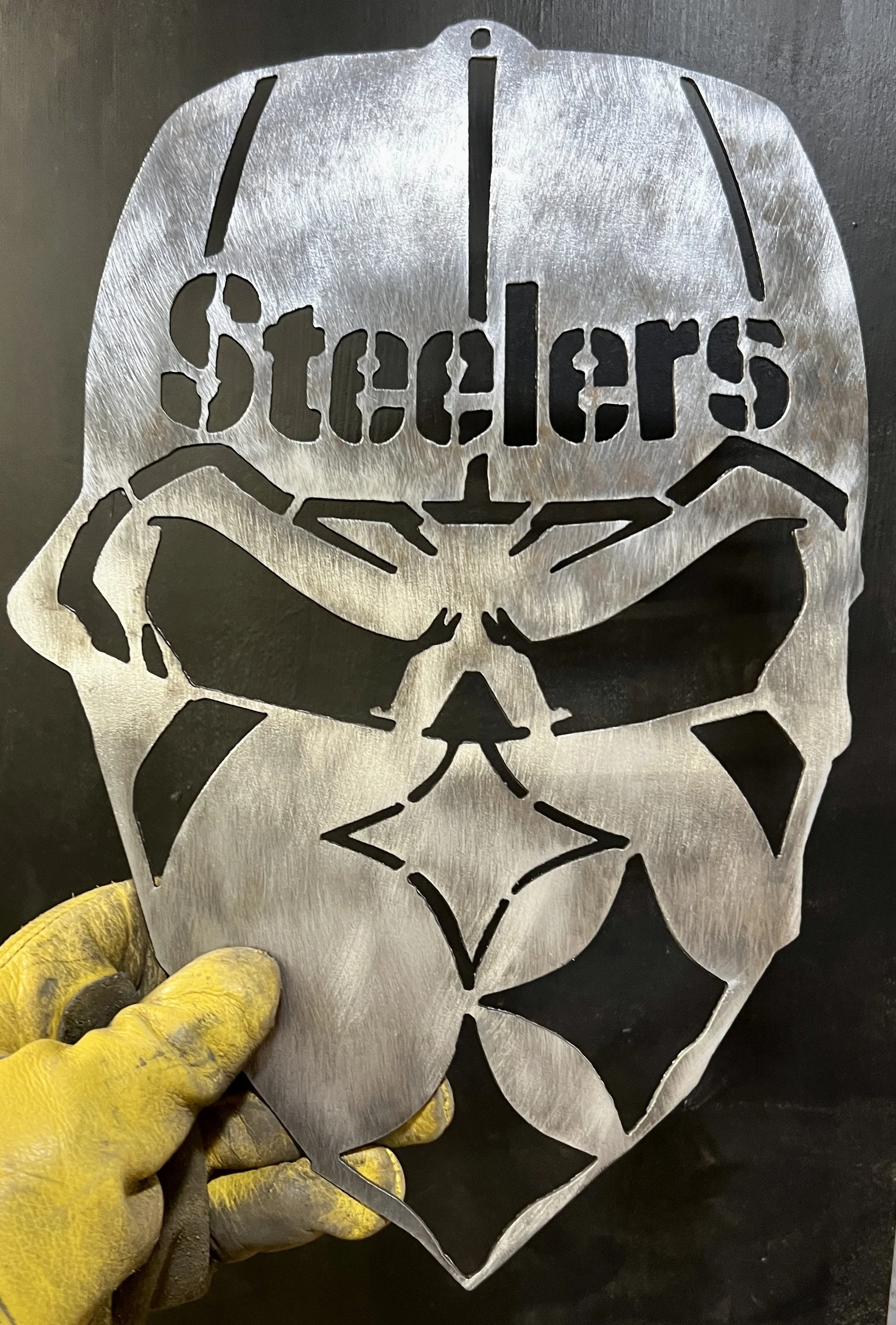 A metal stencil with a Star Wars Stormtrooper helmet design and the word 'STORMTROOPERS' cut out, being held by a person wearing yellow gloves.