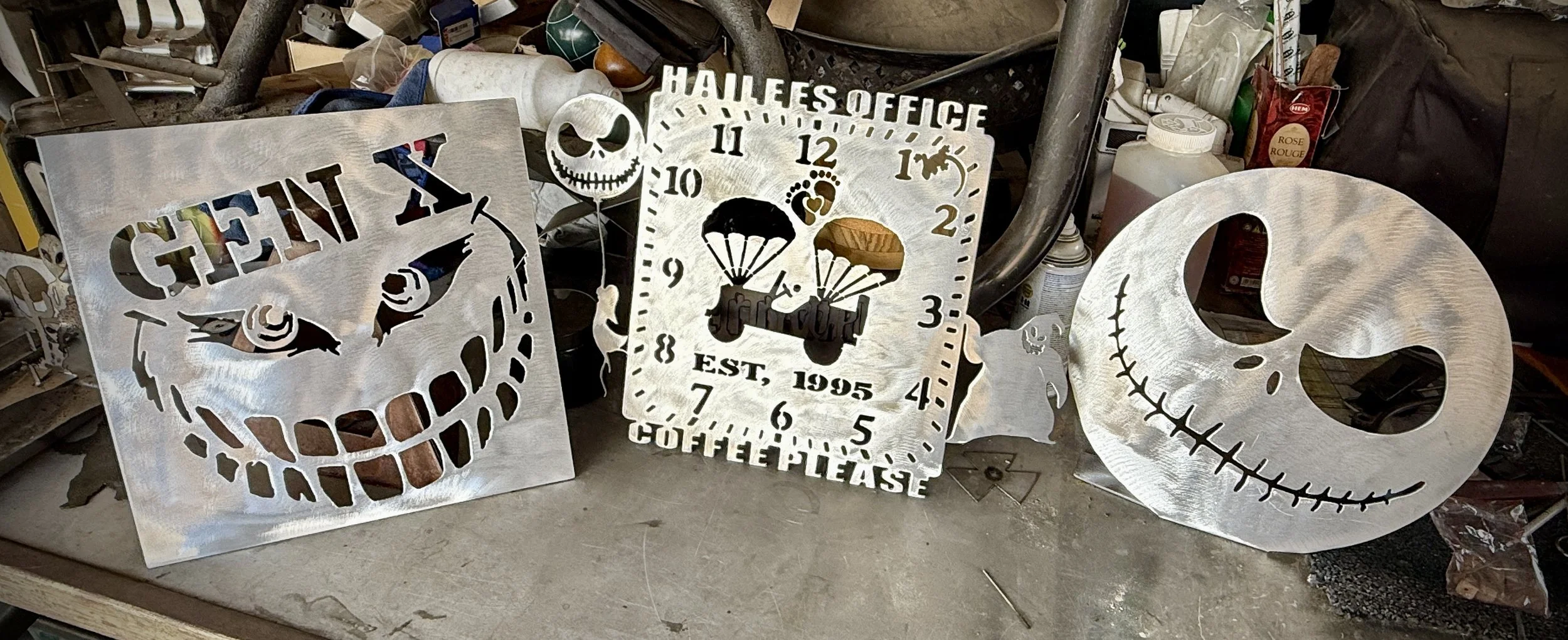 Three metal wall art pieces with skull and Halloween-themed designs, including a grinning skull and a clock with Halloween graphics.