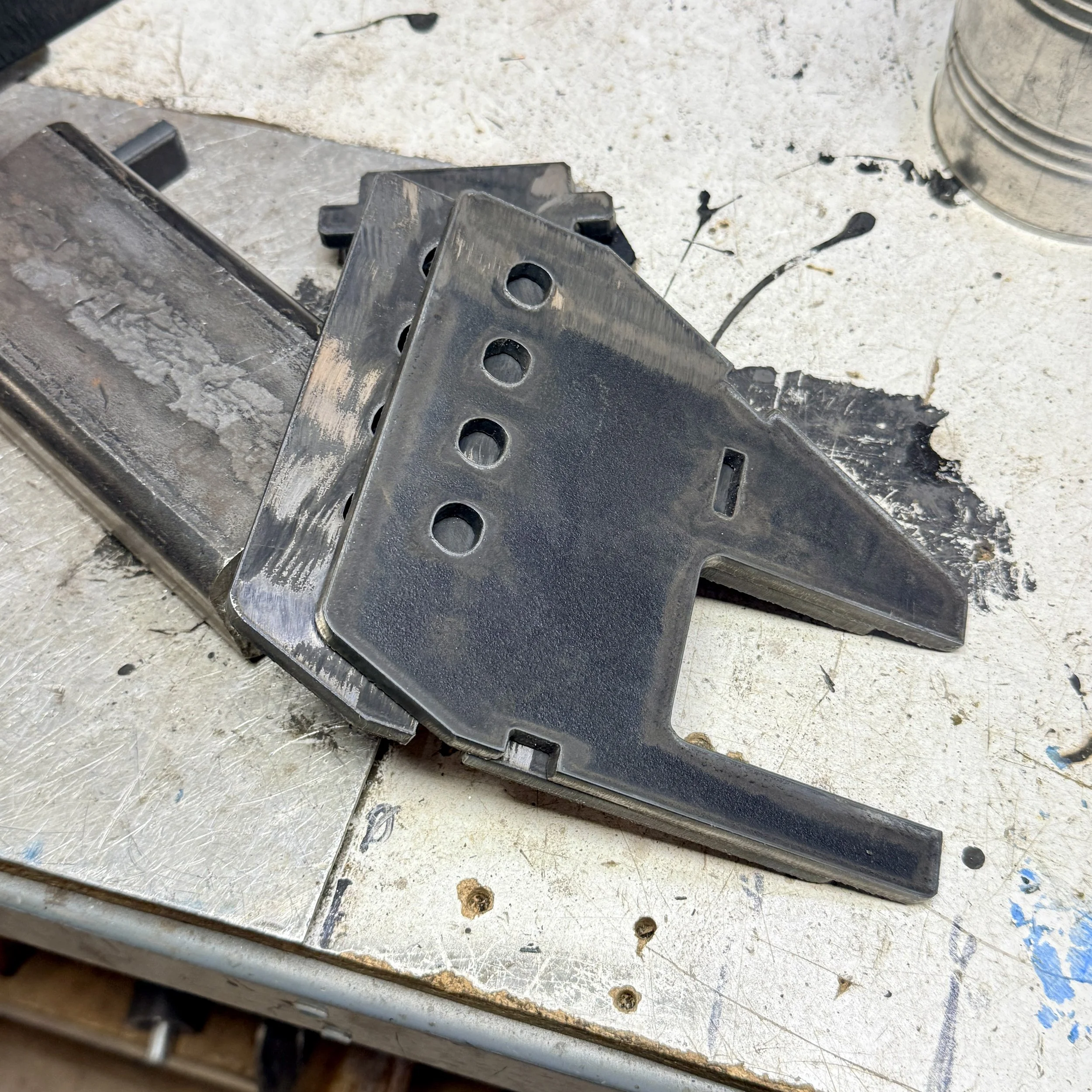 Close-up of metal parts and tools on a workbench covered in dust and debris, including perforated metal pieces and screws.