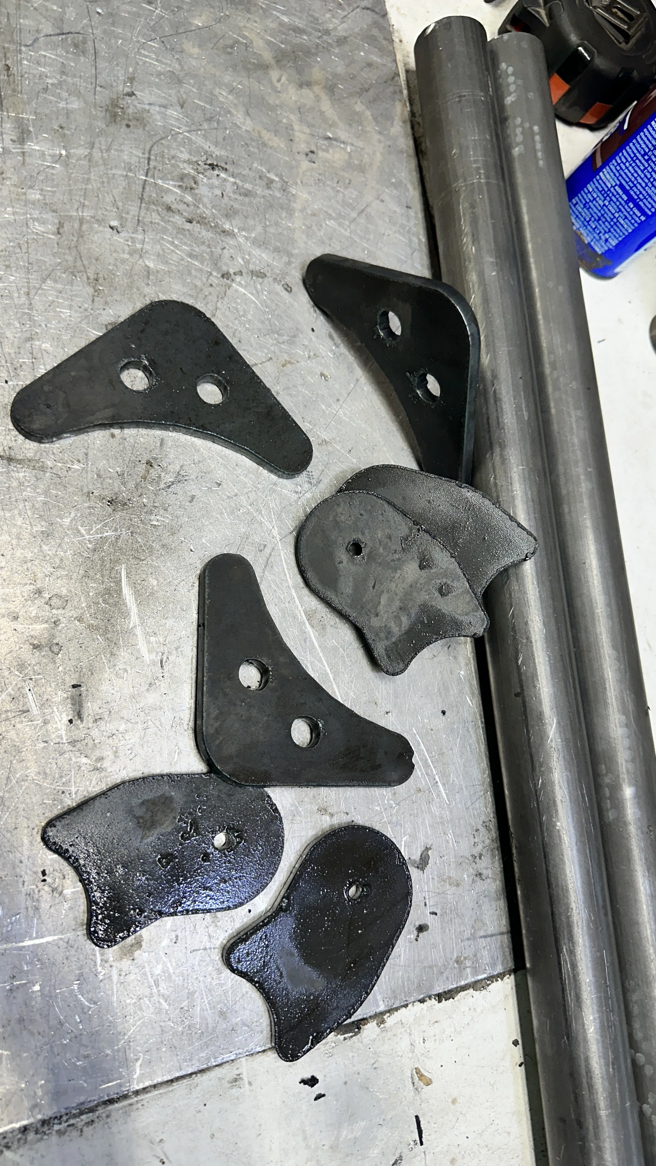 Metal brackets and parts on a workbench in a workshop or garage setting.