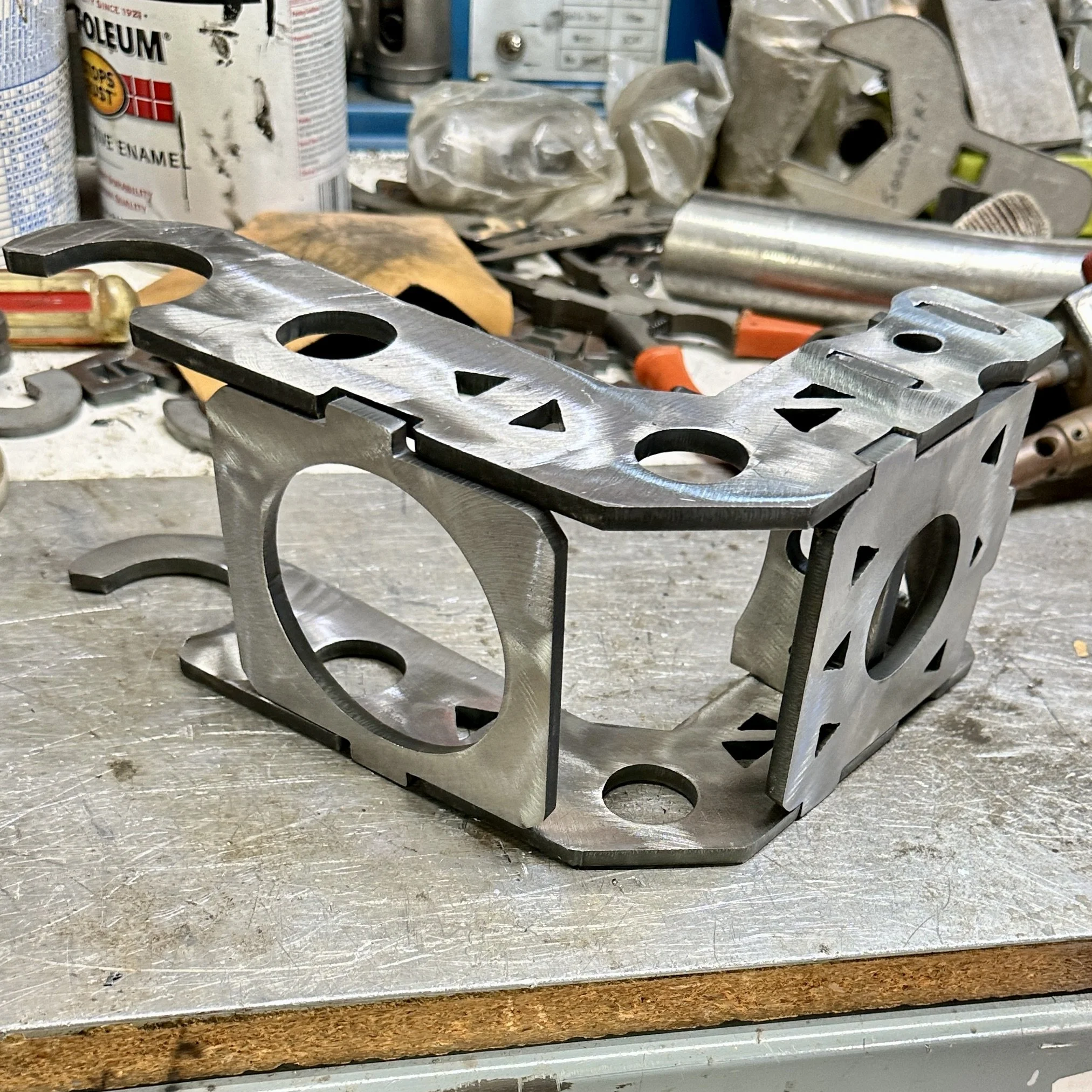 Close-up of a metal workbench with various tools and materials, including metal parts, a level, plastic bags, and spray cans in the background.