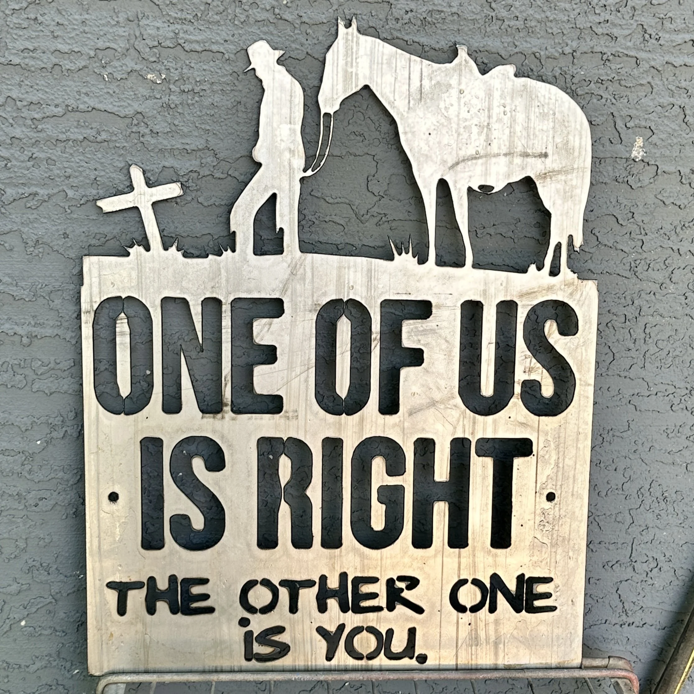 A metal cutout sign on a concrete wall that depicts an elephant with a cross and the words "The others one is you."