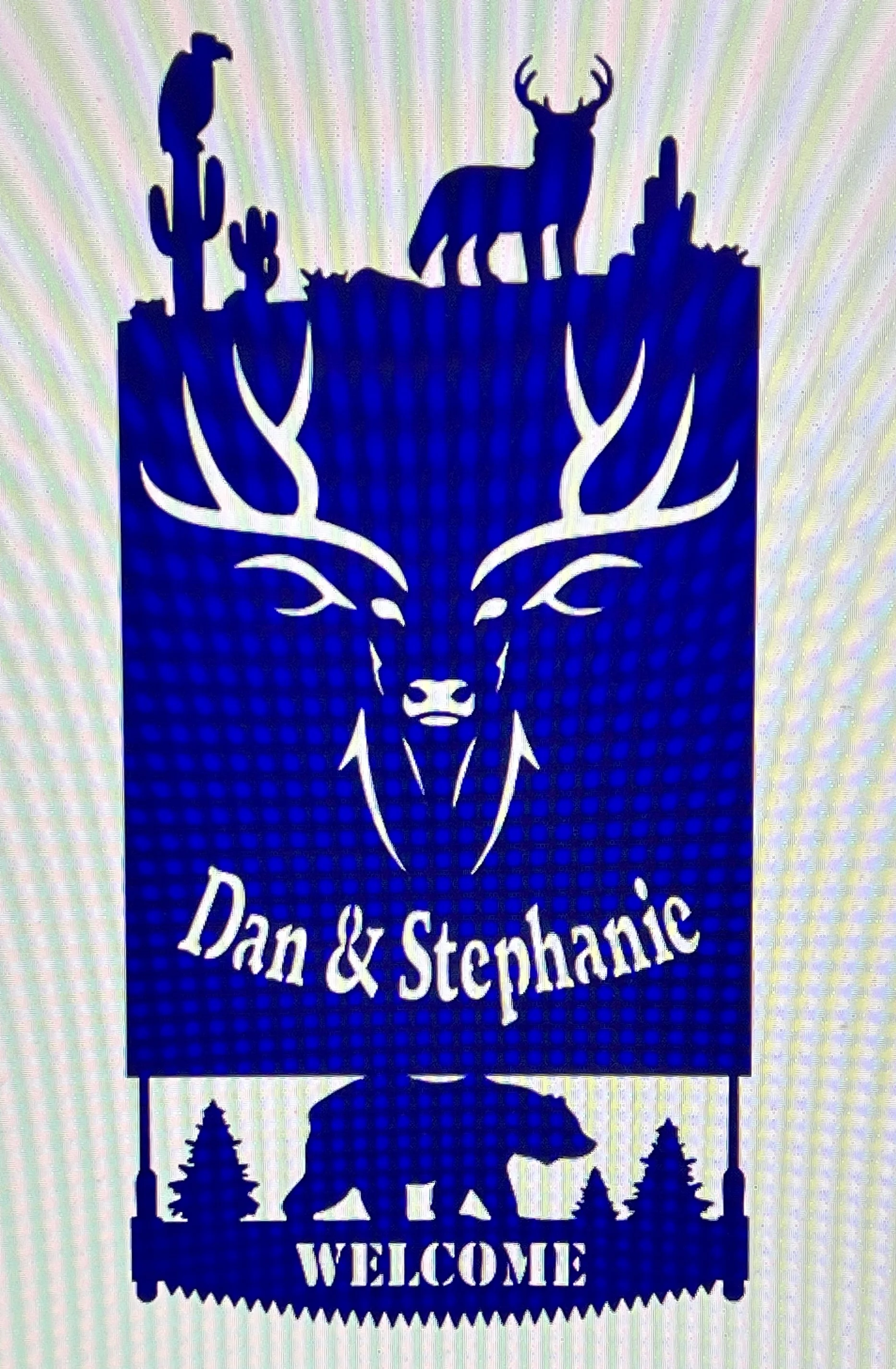A decorative sign with Christmas trees, a bear silhouette, and mountain scenery with pine trees. The sign says, 'Dan & Stephanie' and 'WELCOME'.