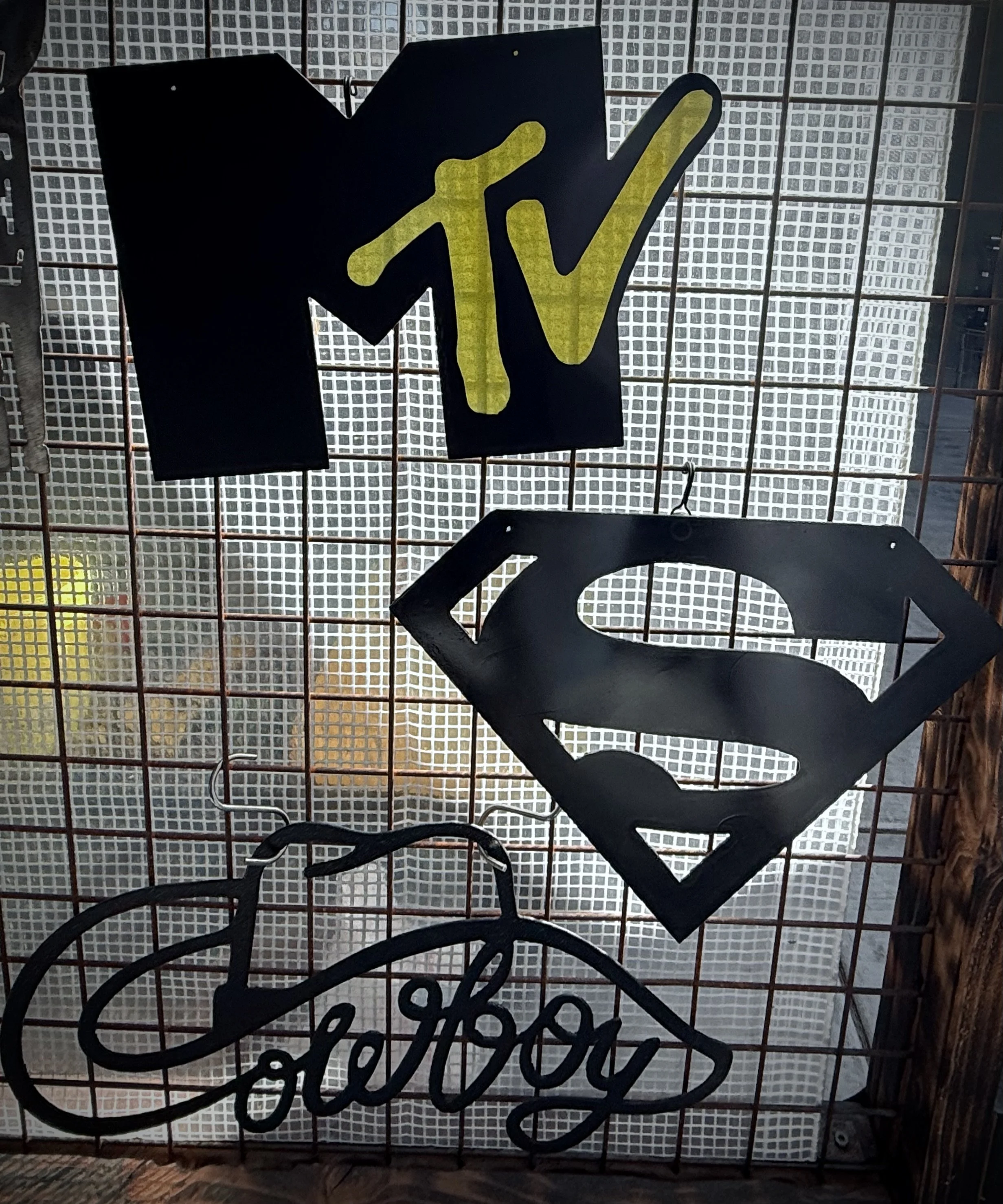 Close-up of a neon sign with the MTV logo, featuring yellow and black colors, mounted on a metal grid background.