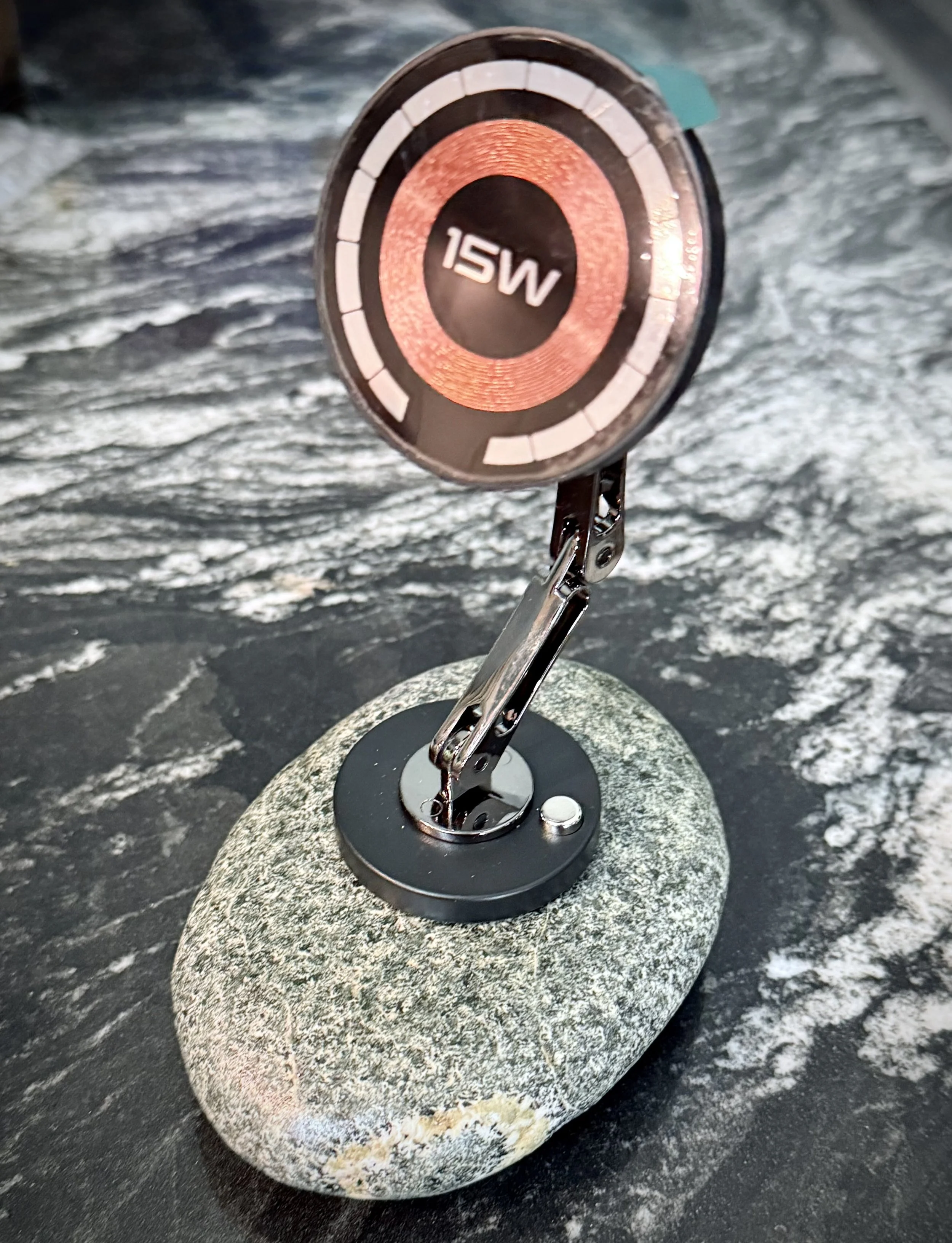 Close-up of a marine navigation equipment device with a 15W power rating, mounted on a rounded stone base on a boat, with water in the background.