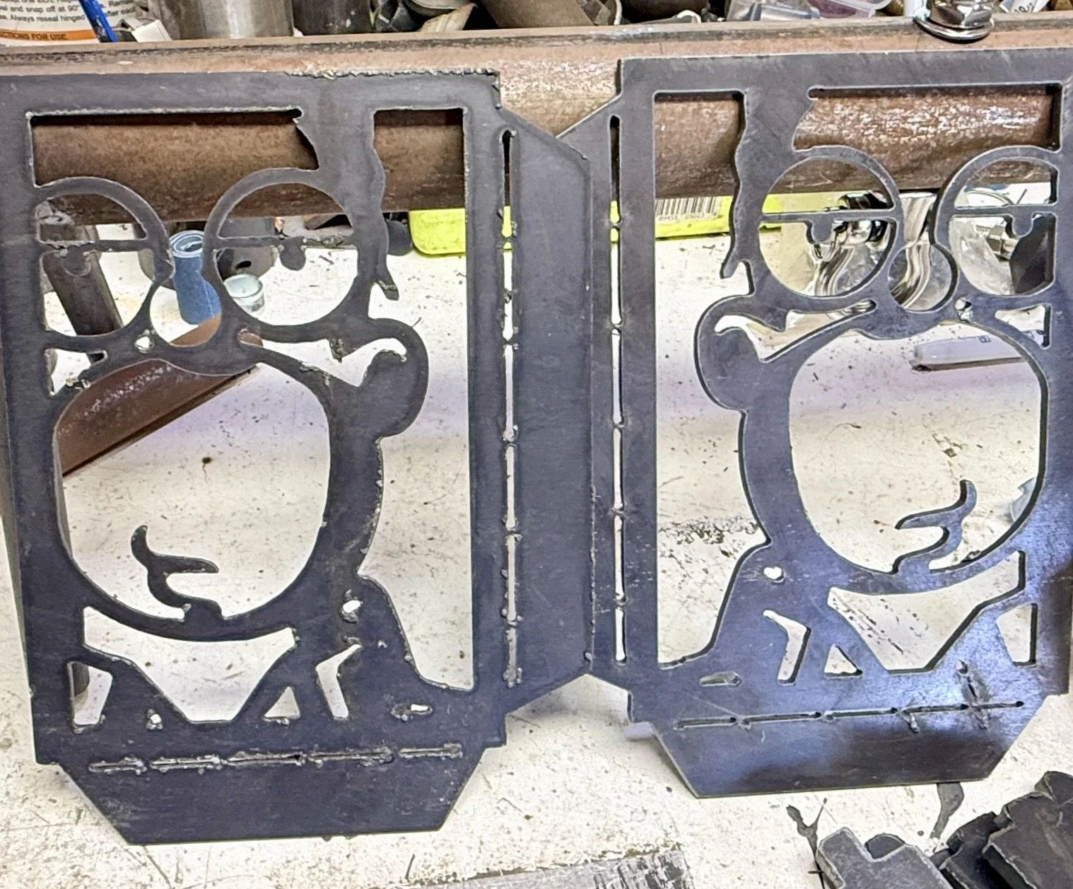 Metal decorative panel with silhouettes of children playing, placed in front of a workbench with tools and supplies in the background.