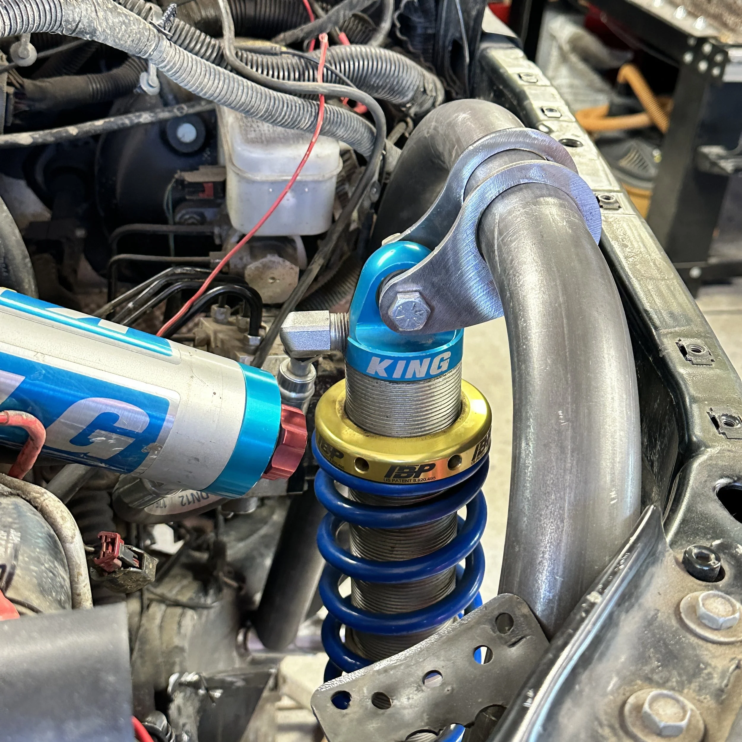 Close-up of a vehicle suspension system showing a blue coil spring and metallic parts, with other engine and wiring components visible.