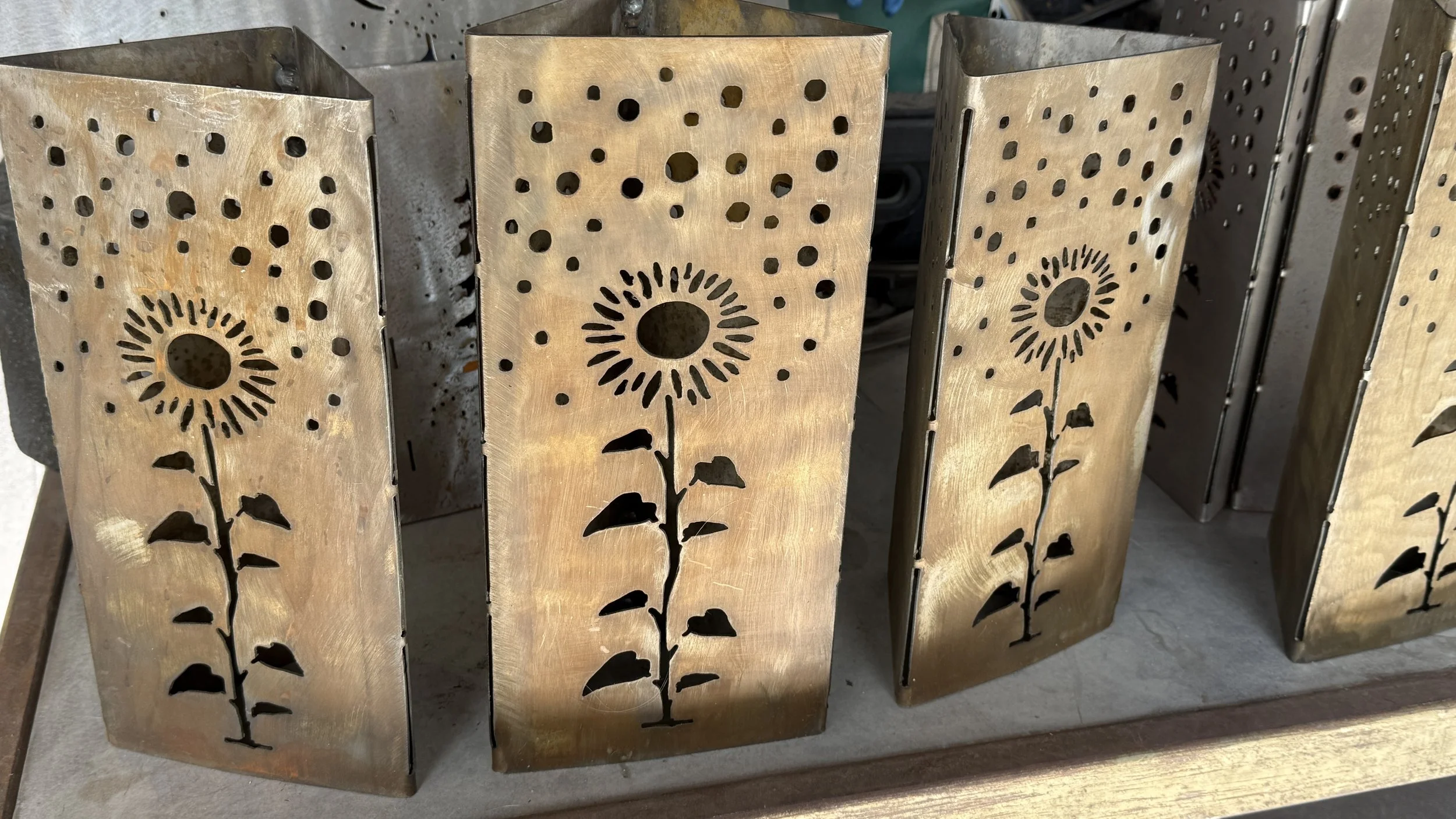 Metal lanterns with flower and stem cutouts sitting on a wooden surface.