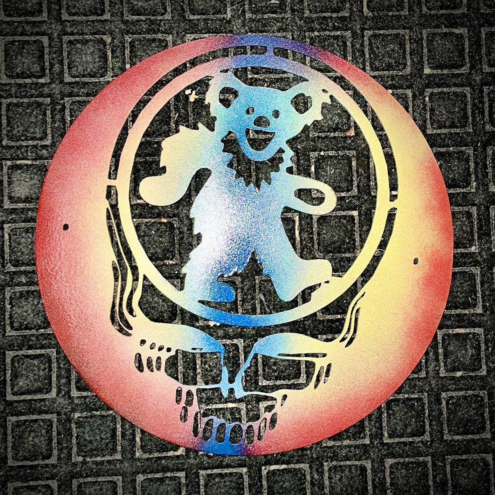 A metal art piece of a skull with a dog's face inside, held in a red circle, on a black textured surface.