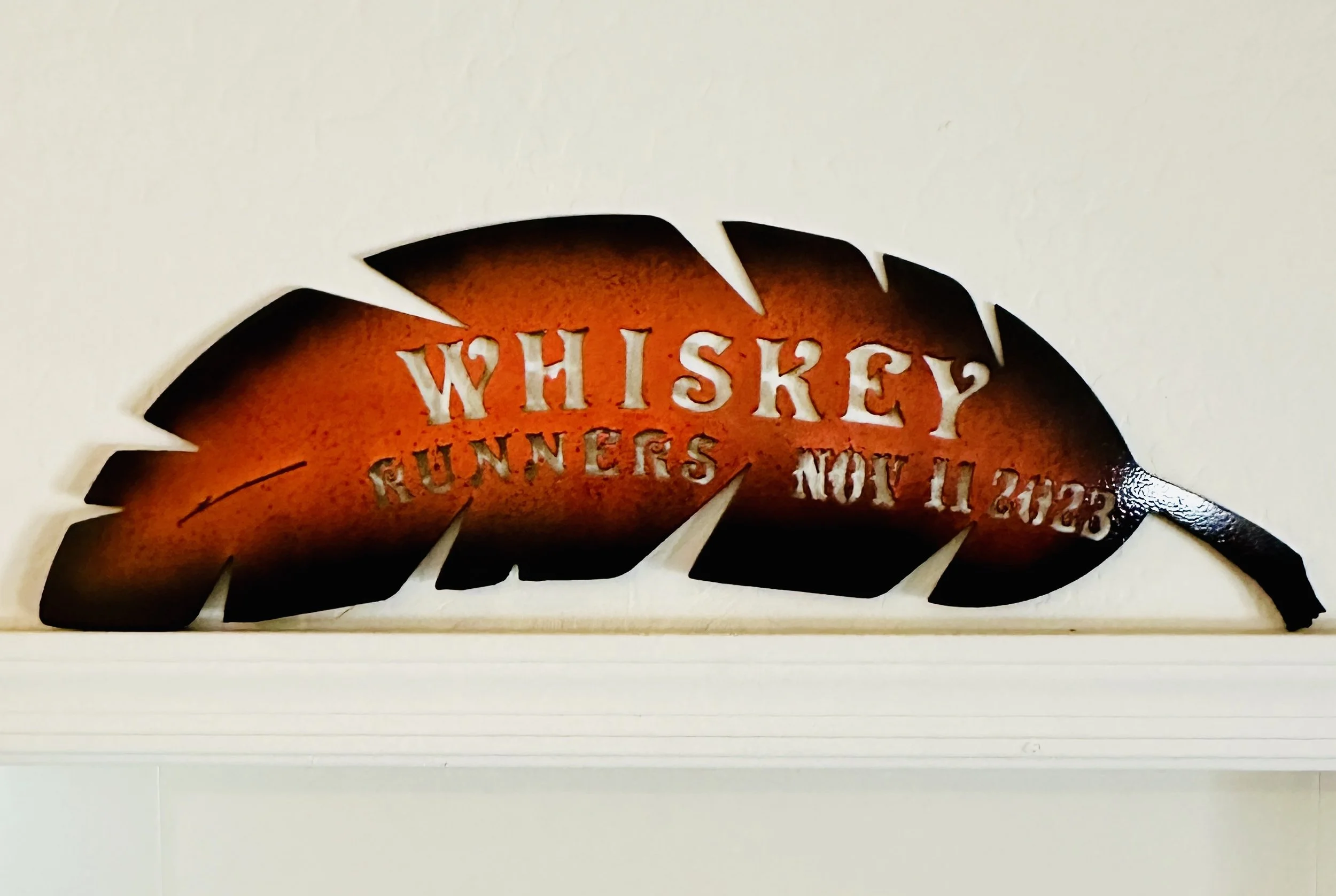 Decorative wall art featuring a cut-out of a fish with the words 'Whiskey Sunters' and additional unreadable text inside, mounted on a white wall.