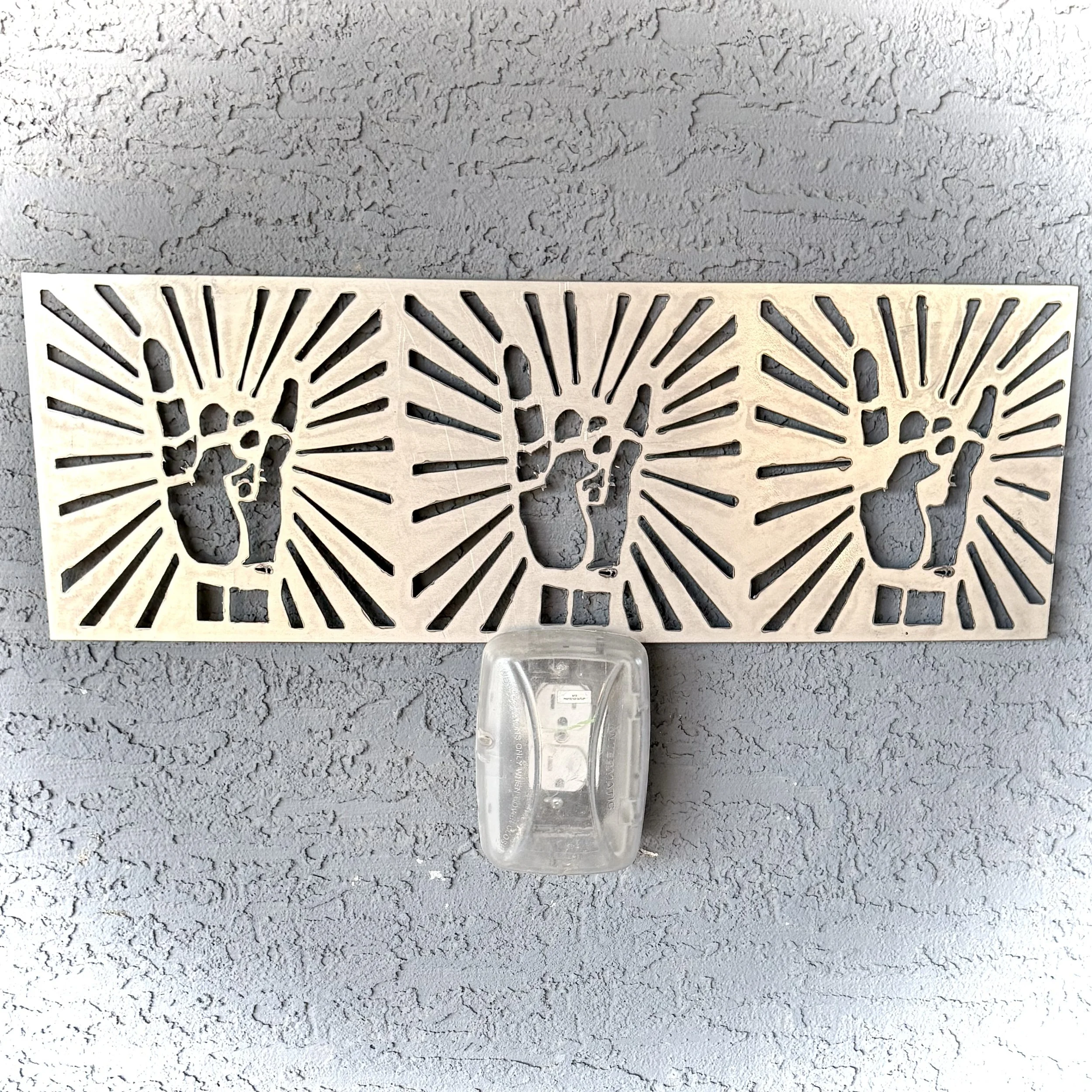A clear plastic bottle and a decorative cut-out panel with radial patterns against a textured wall.