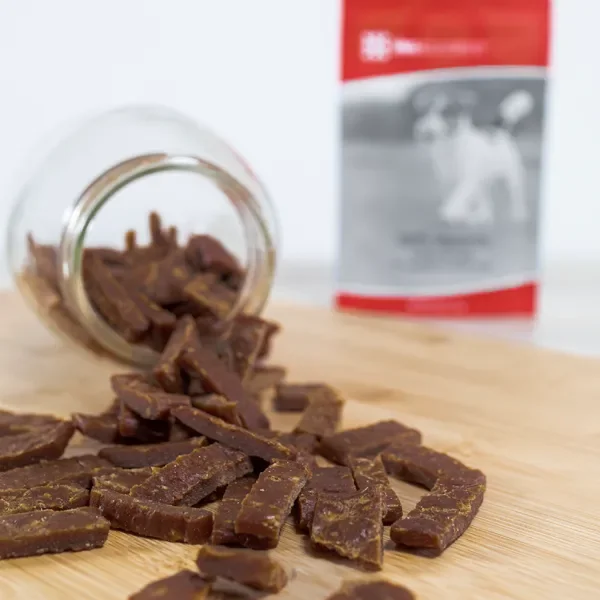 Pieces of chocolate with a jar laying on its side on a wooden surface, and a blurred bag in the background.