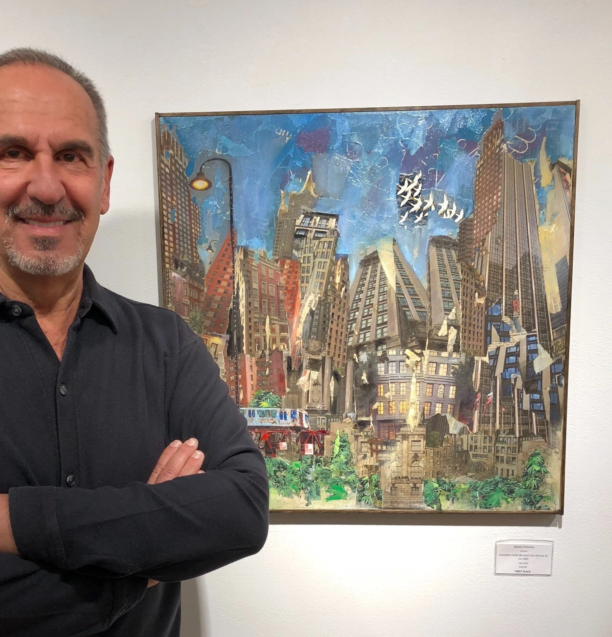 Man with gray hair and beard in black shirt standing next to large artwork depicting a cityscape with skyscrapers, bright colors, and dynamic textures, displayed in a gallery.