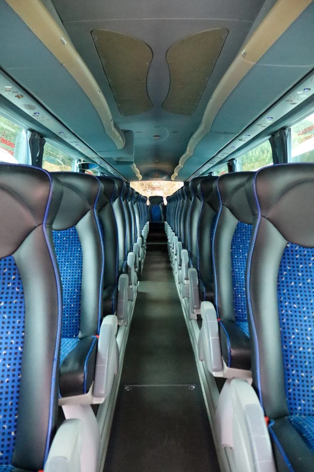 Interior de um ônibus de dois andares, com assentos de couro preto e detalhes azuis, e janelas grandes nas laterais.
