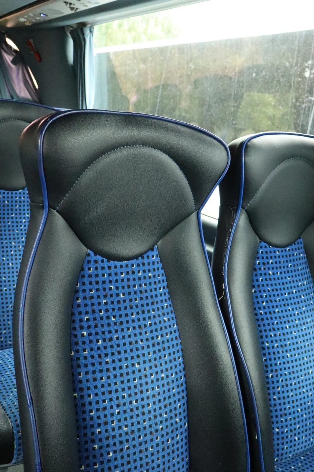 Assentos de ônibus com estofados azuis com detalhes em preto e detalhes azuis nas bordas, vista do interior de um veículo.