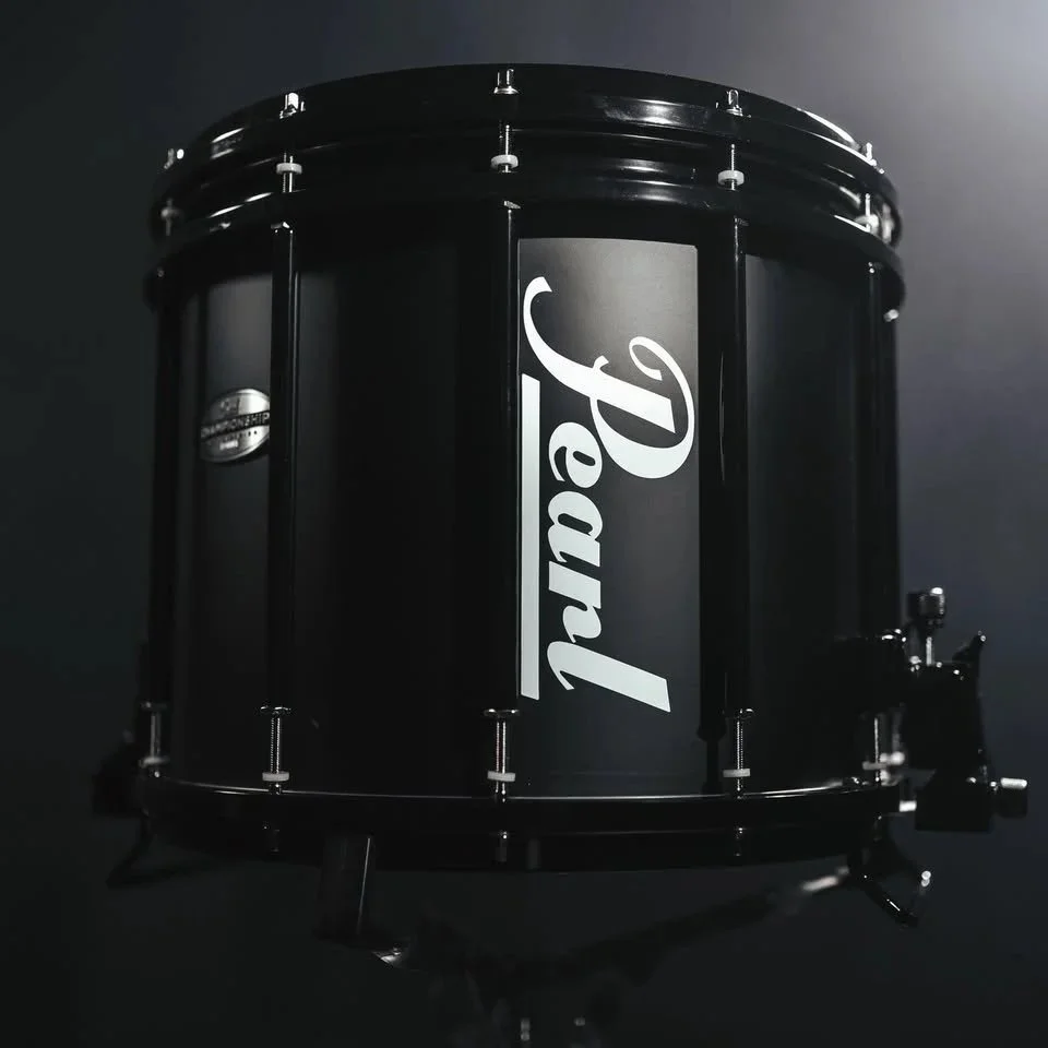 A black Pearl drum with a white Pearl logo on the side, mounted on a stand, against a dark background.