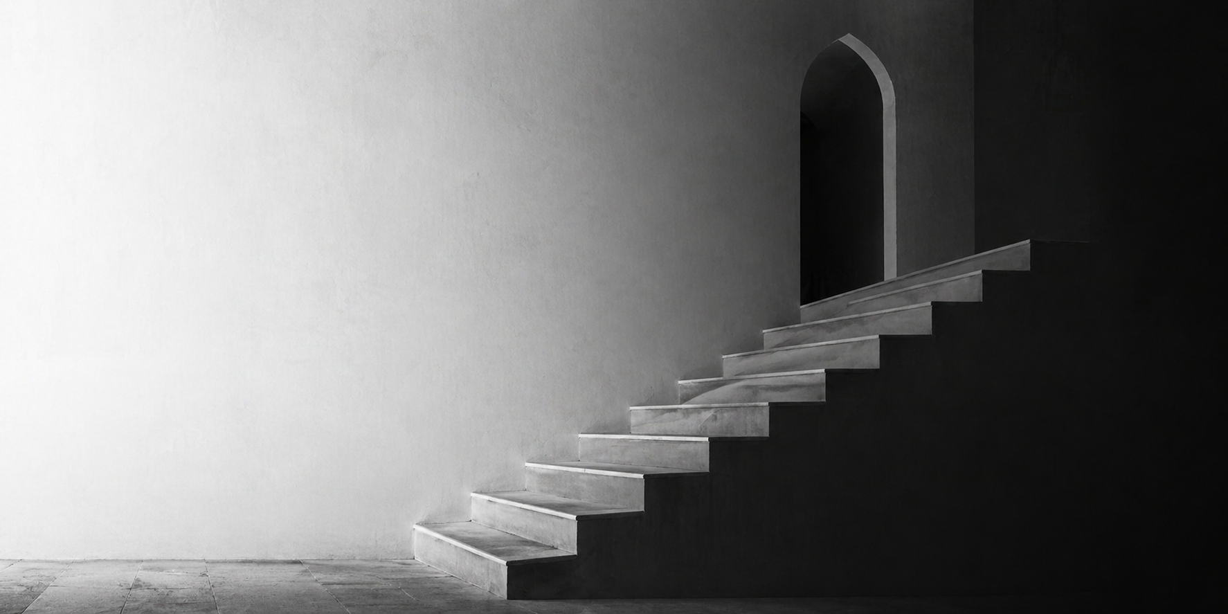 A minimalist black and white staircase with steps leading to an arched doorway in a dark wall, contrasting against a plain light-colored wall.