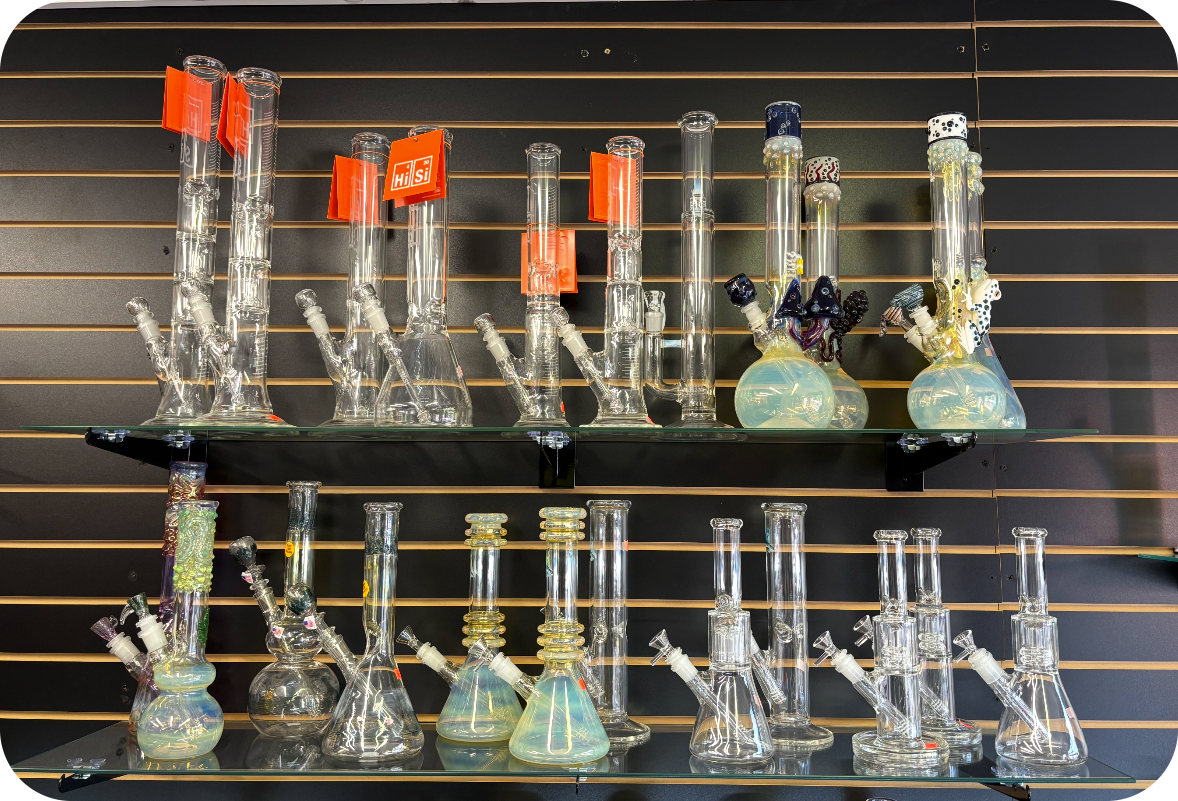 Display of various glass bongs on black shelves against a black slatted wall.