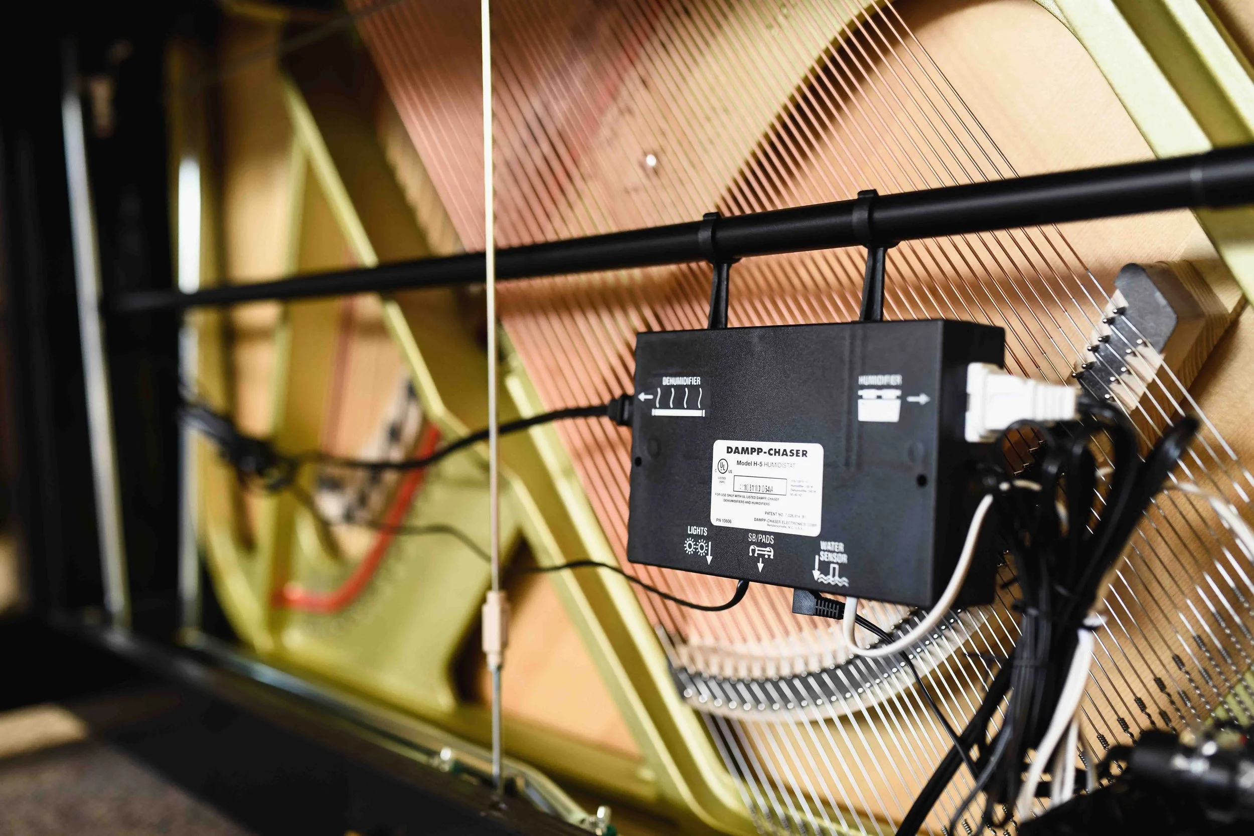 Close-up view of a piano's interior strings and an electronic humidifier device attached to the strings.