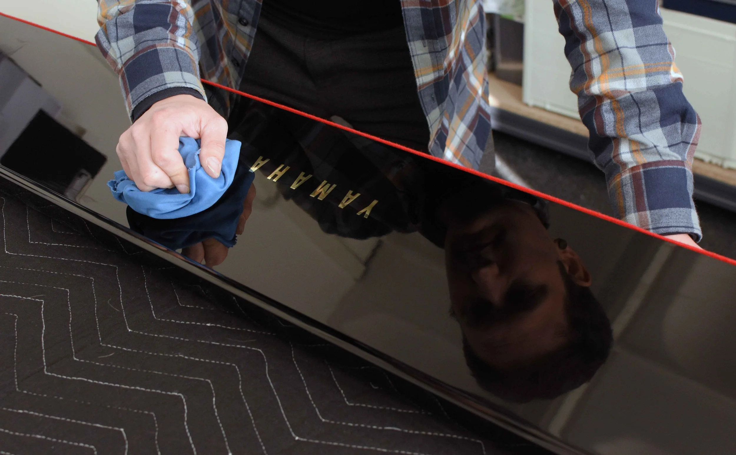 Person cleaning a reflective black piano key lid with a blue cloth.