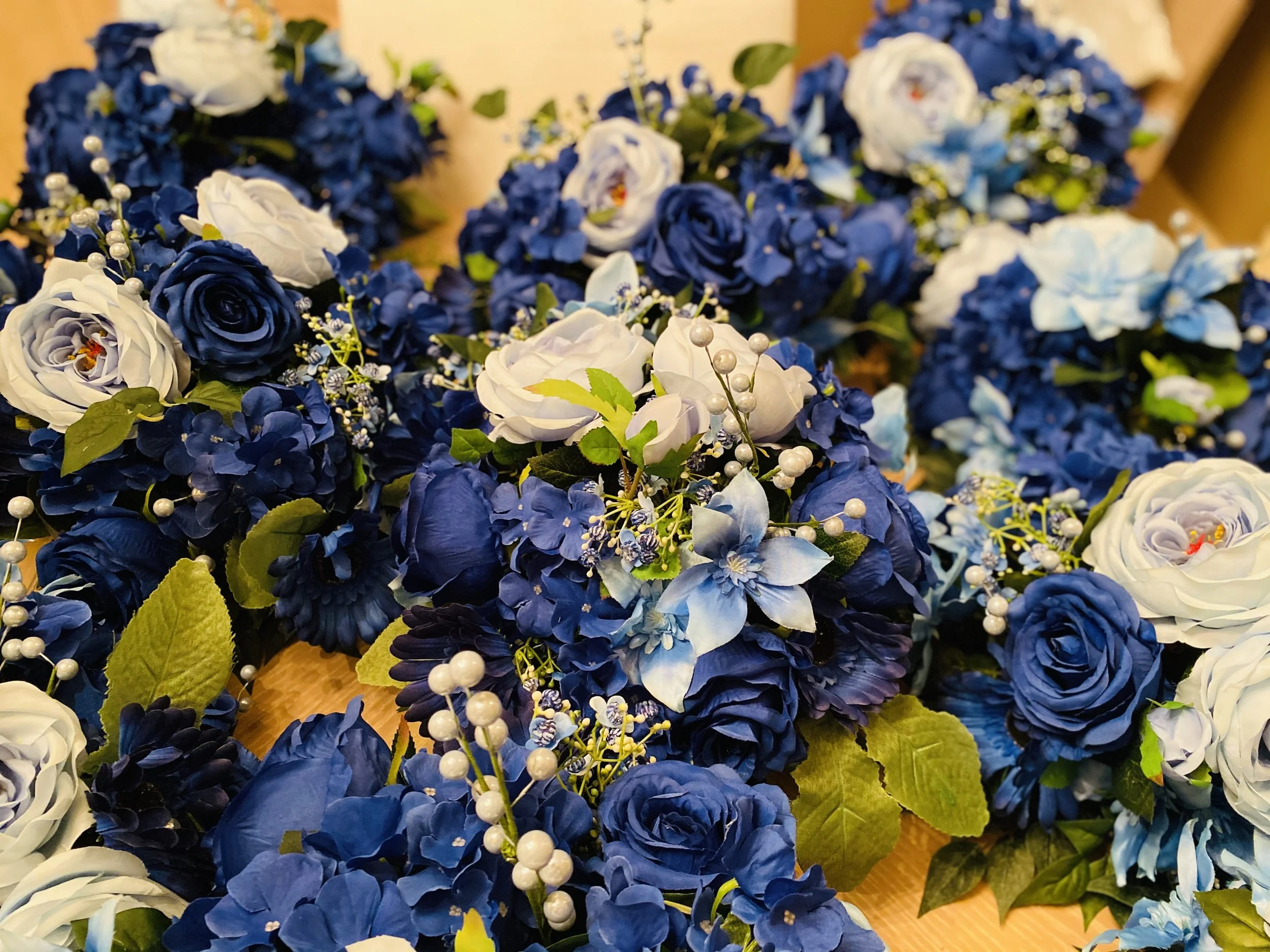 Close-up of a floral arrangement with blue and white flowers, green leaves, and decorative white pearl-like accents.