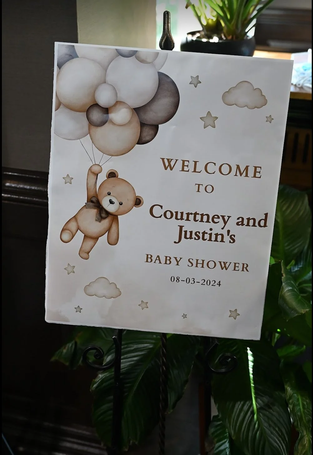 Baby shower welcome sign with teddy bear holding balloons, clouds, stars, and soft colors, welcoming Courtney and Justin with the date 08-03-2024.