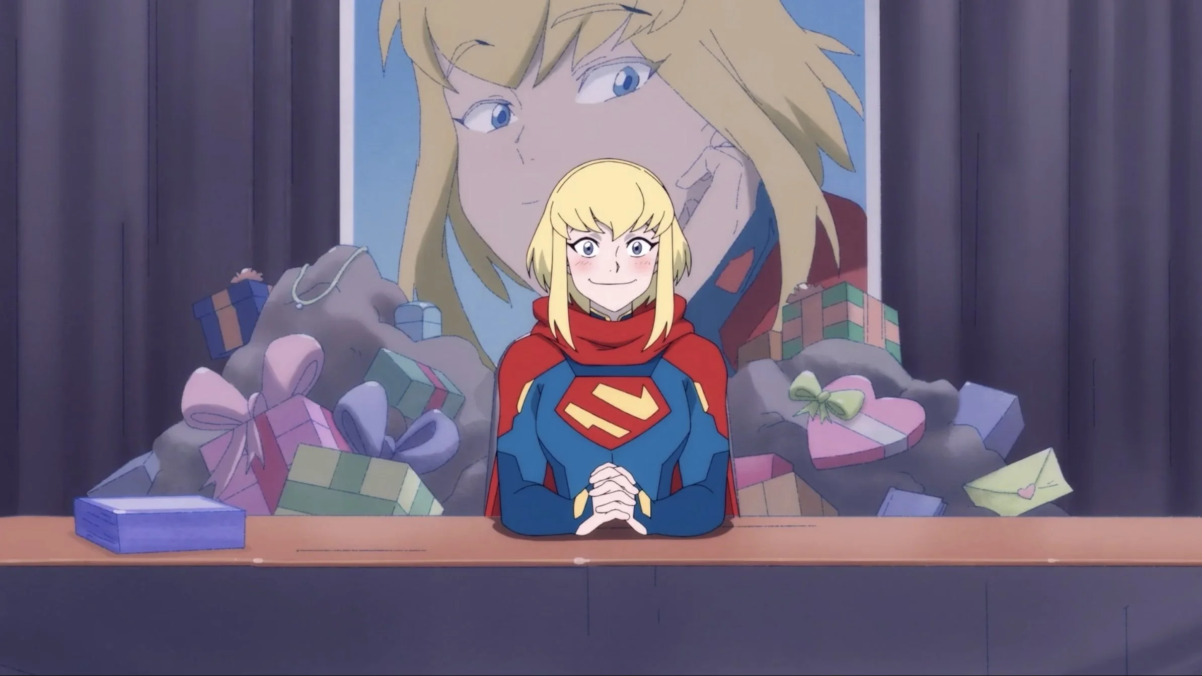 A screen grab from the series, showing Kara sat at a convention booth with the most precious smile and blushing face, as gifts are piled up behind her.