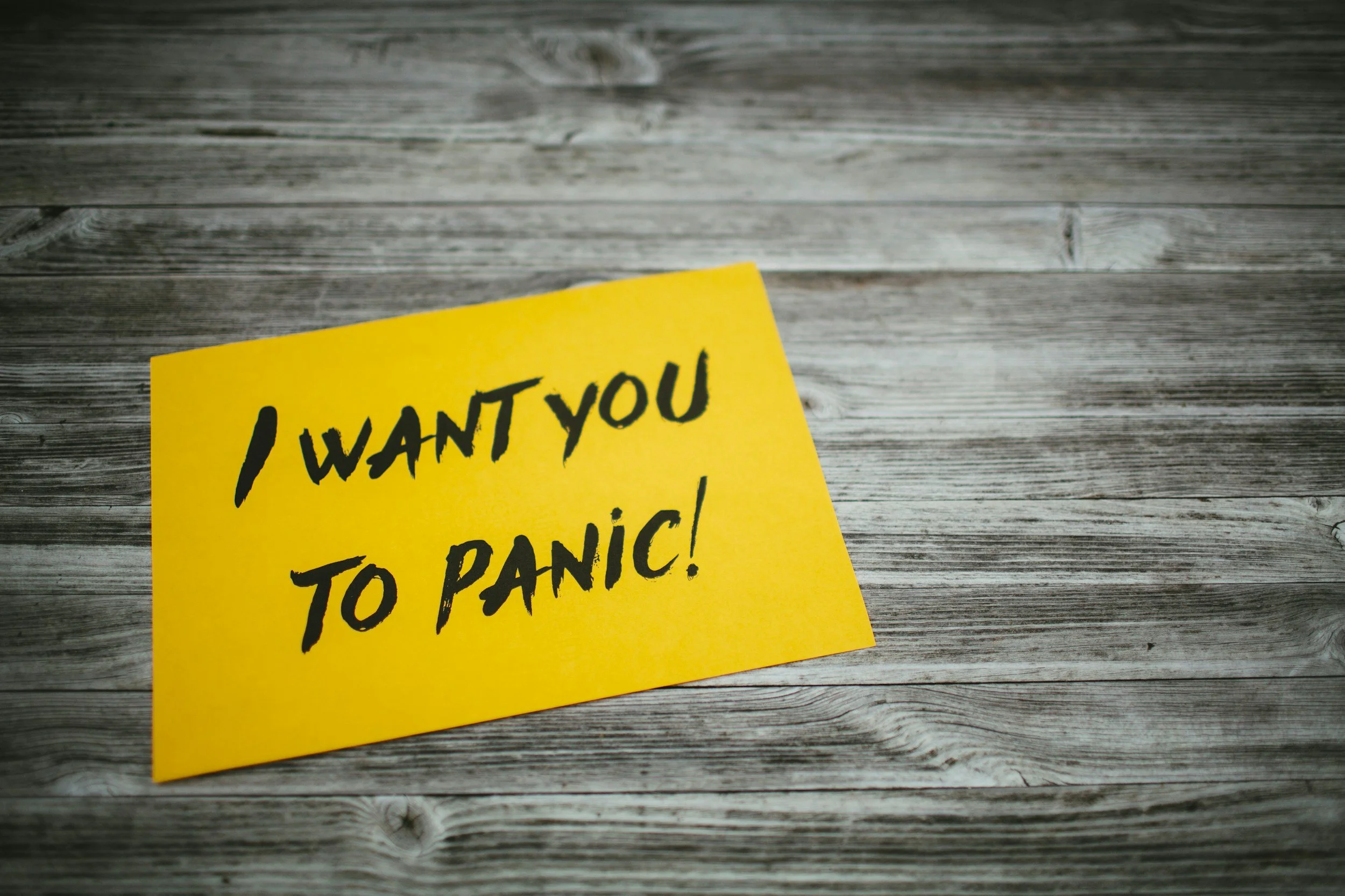 A yellow handwritten note that says "I WANT YOU TO PANIC!" on a wooden surface.
