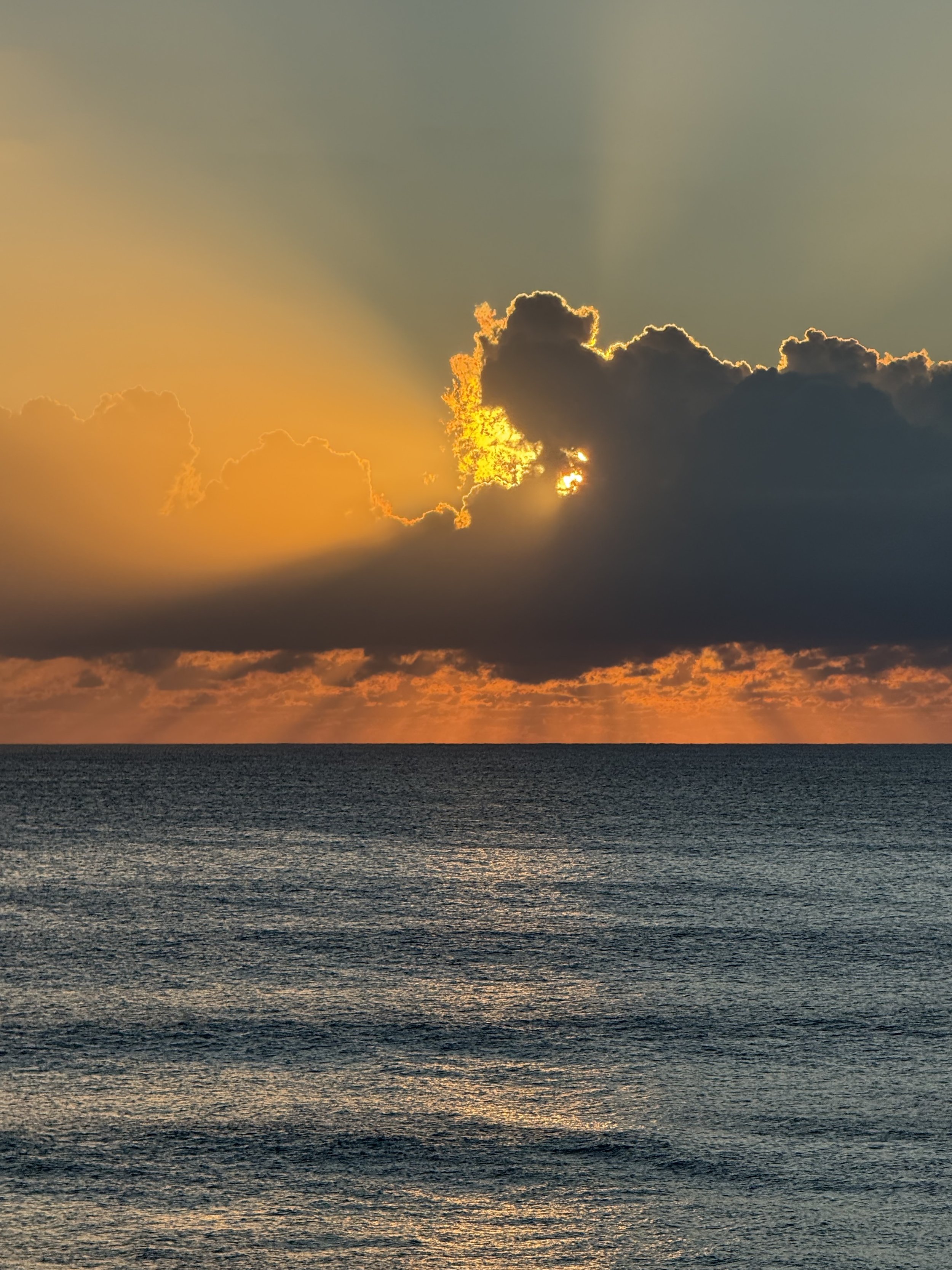 Sunset over the ocean with clouds partially blocking the sun.